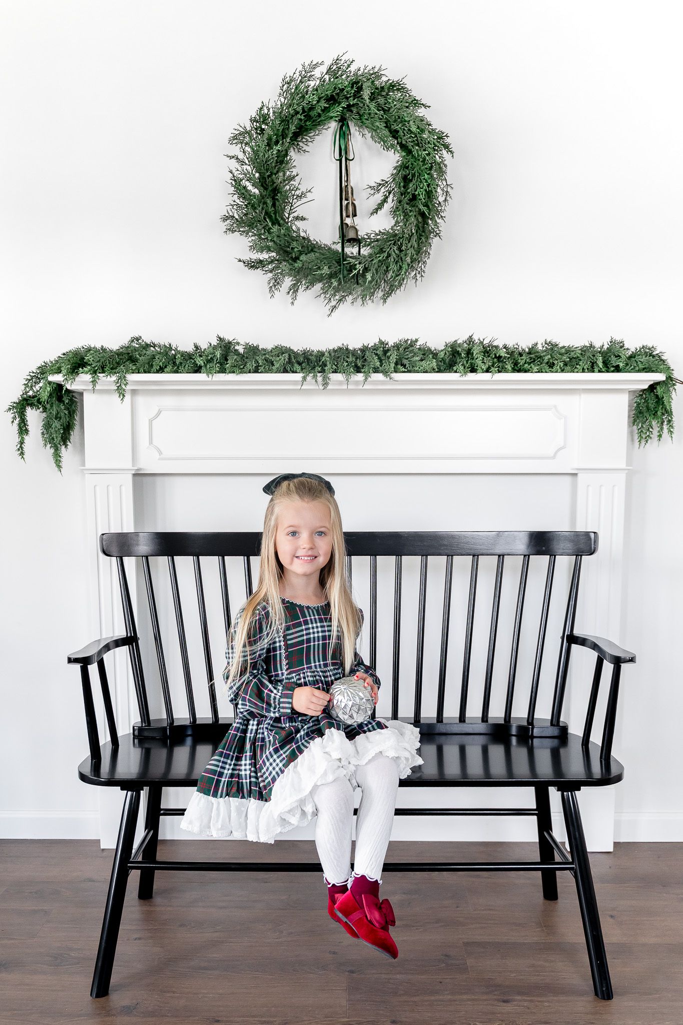 Black wooden bench decorated with evergreen wreaths and holiday decor in bright interior setting.