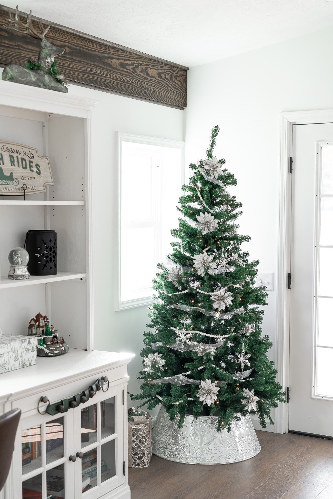 A decorated Christmas tree stands in a modern farmhouse-style room with white walls.