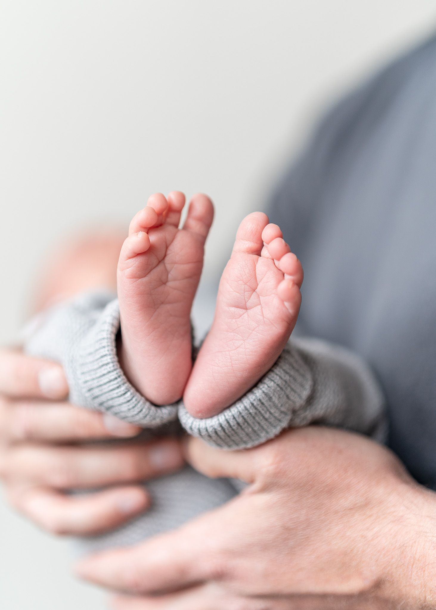 Tiny newborn baby feet wearing gray knitted booties held gently in adult hands.