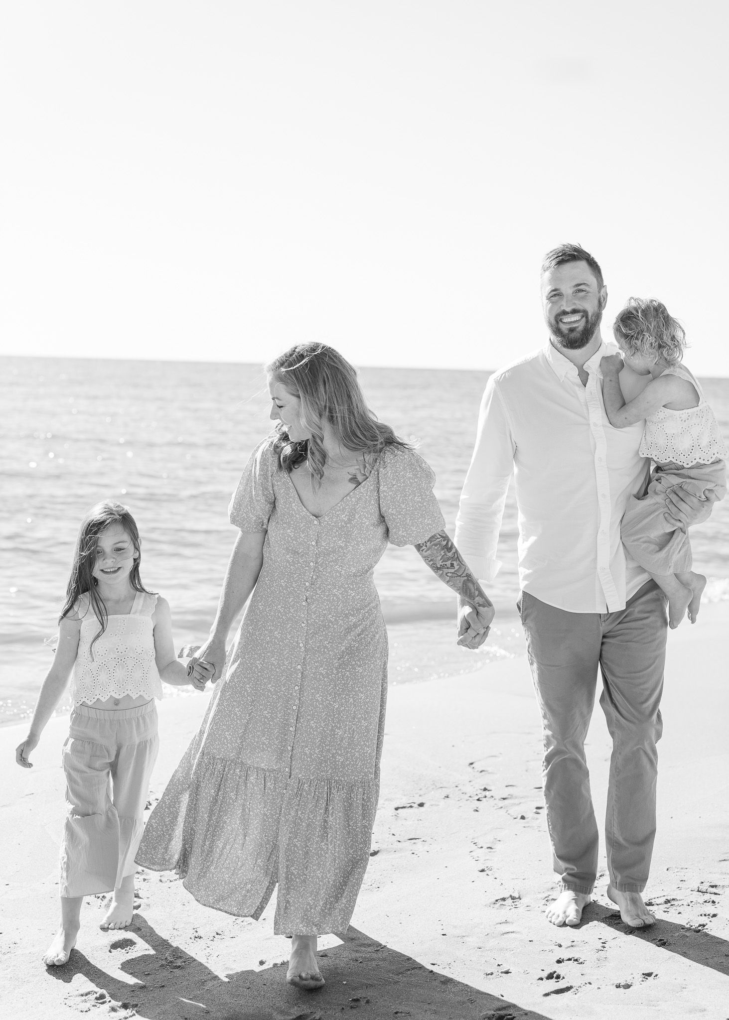 A couple shares joyful moments together walking and playing on a sunny beach in black and white photography.