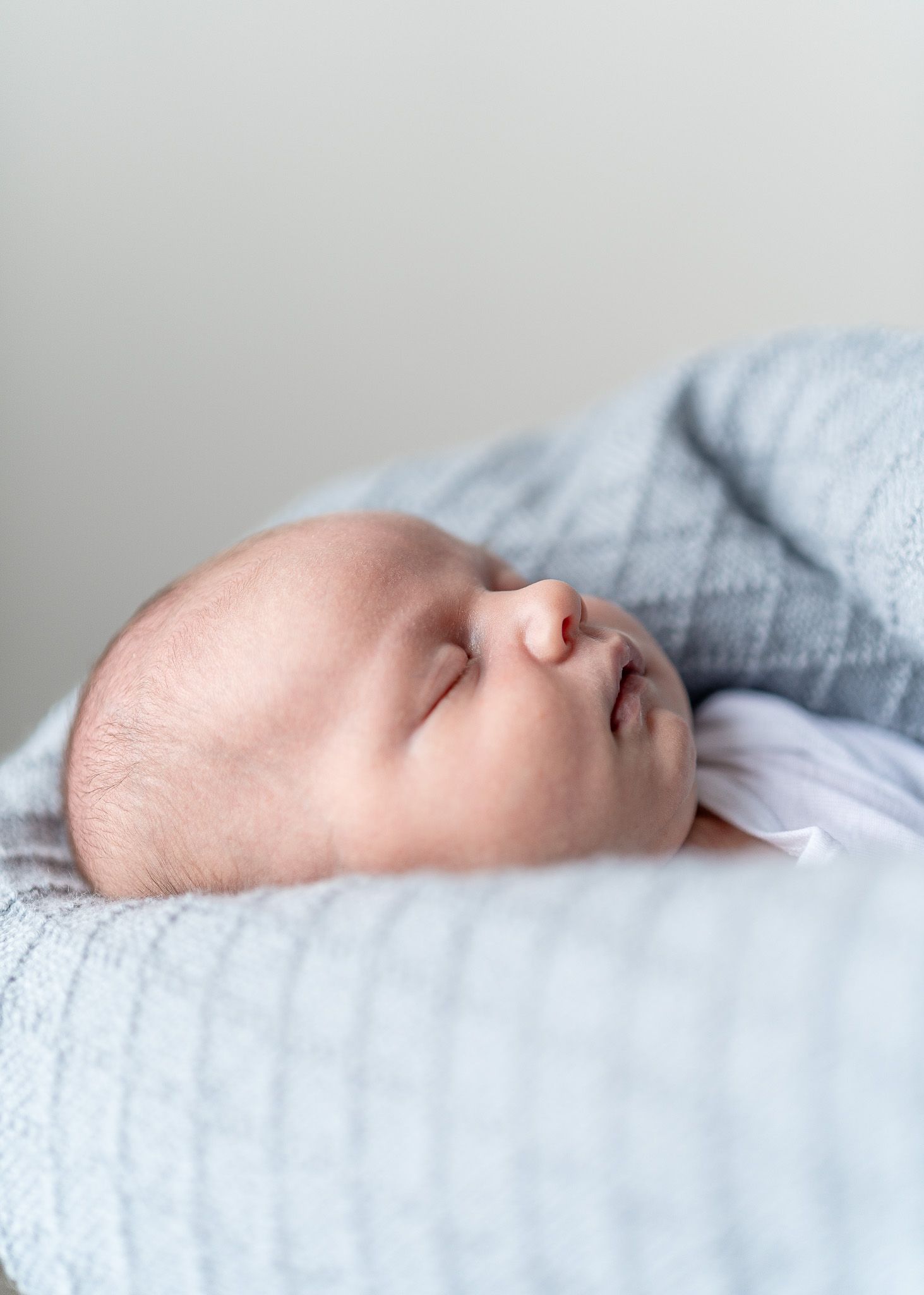 A peaceful sleeping baby rests on soft white and blue bedding in a serene portrait.