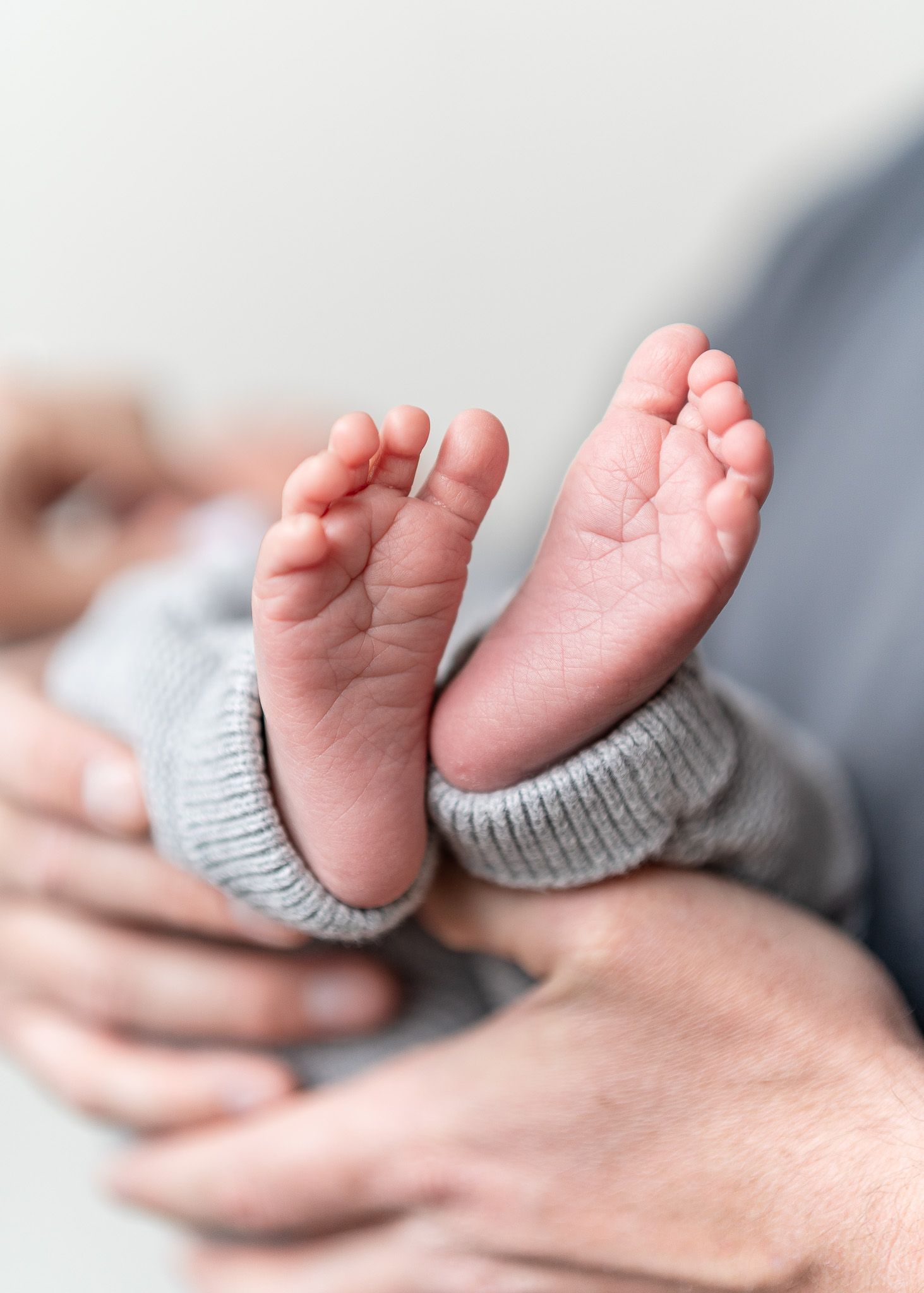 Tiny newborn baby feet resting gently in adult hands wearing a soft gray knit sweater.