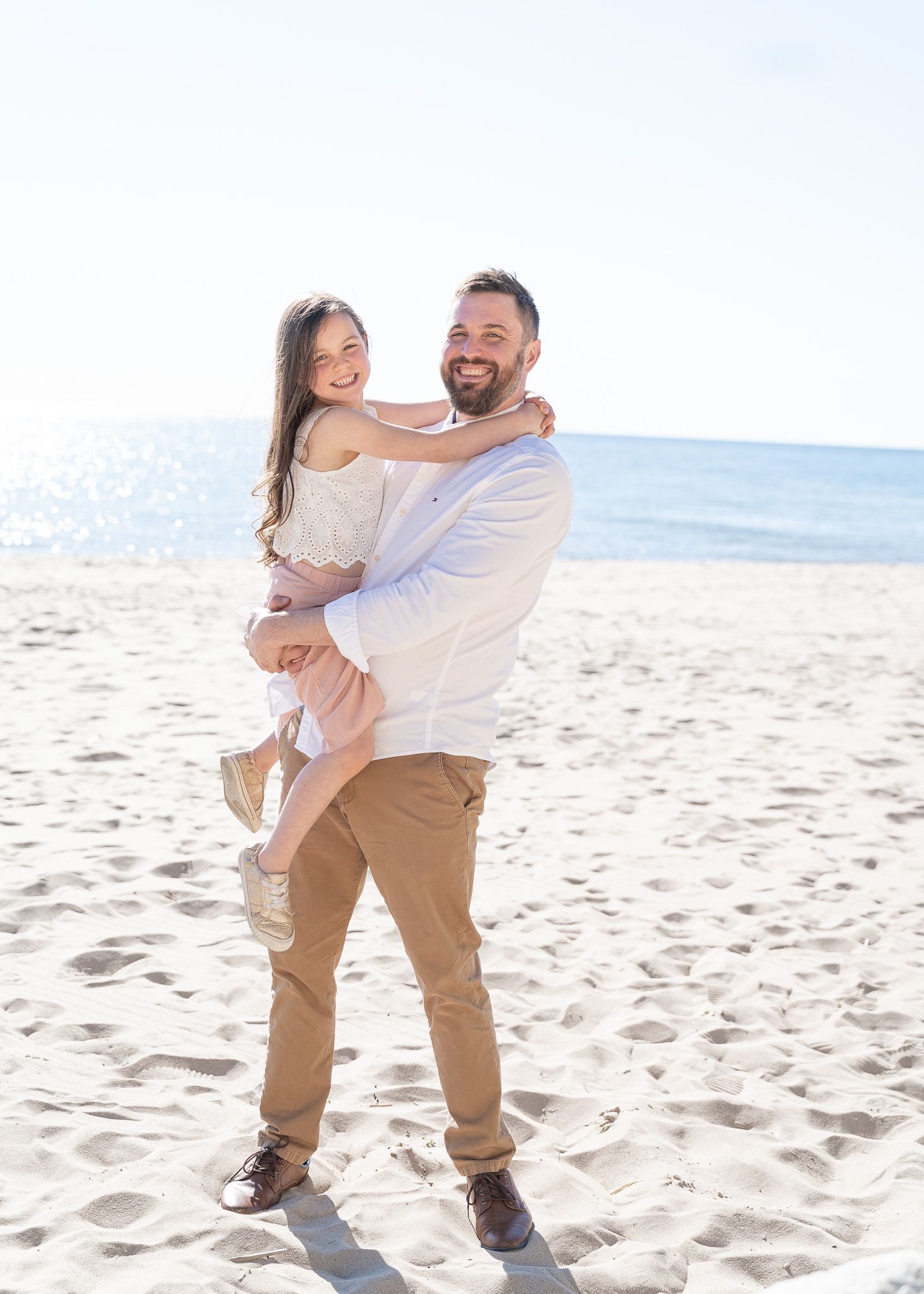 A joyful moment captured on a sunny beach with two people embracing and laughing together by the ocean.
