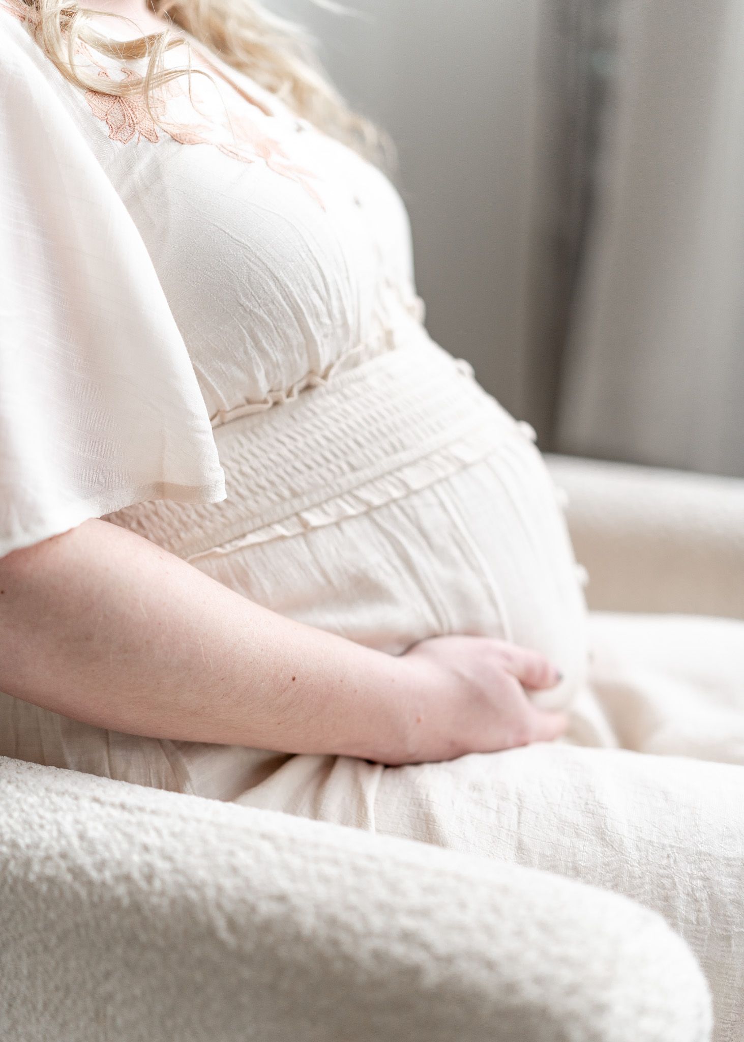 Close-up shot of a pregnant woman's belly in a white lace dress against a light background.