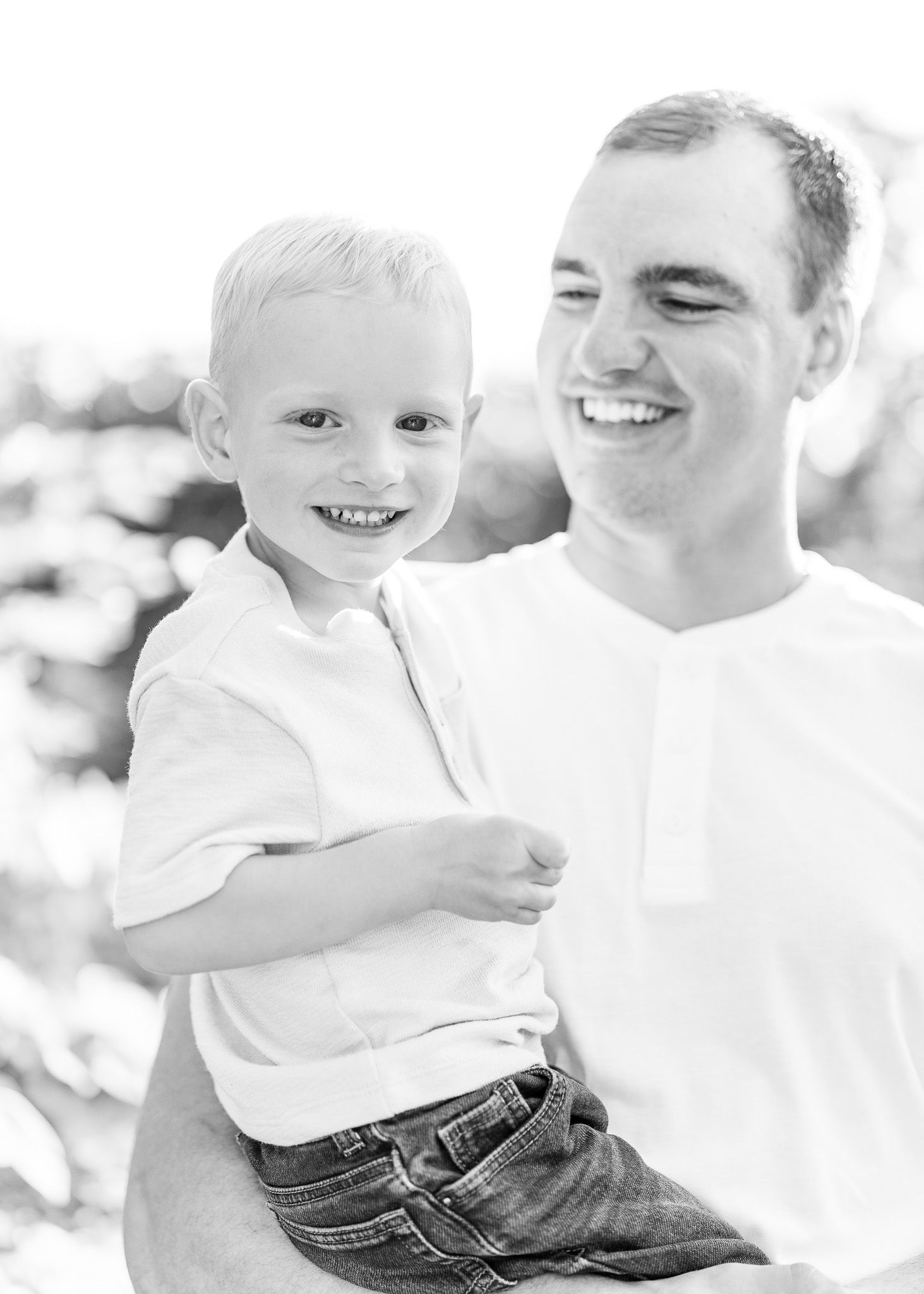 A black and white portrait of a parent and child smiling together outdoors in casual attire.