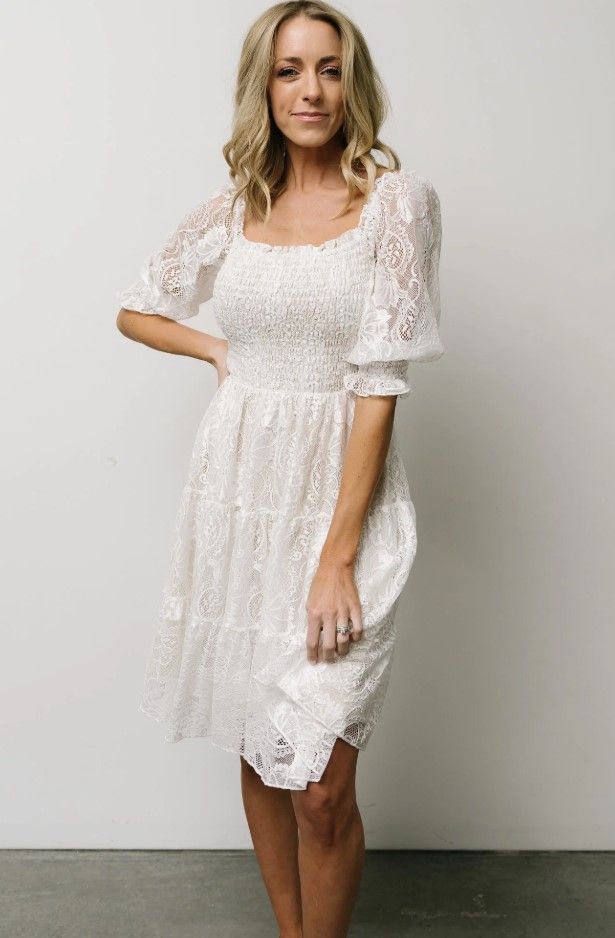 White lace babydoll dress with puff sleeves modeled against neutral background.