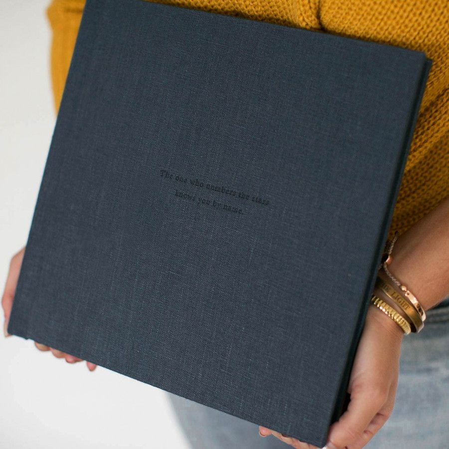 A dark gray linen-bound book or photo album held against a mustard yellow background.