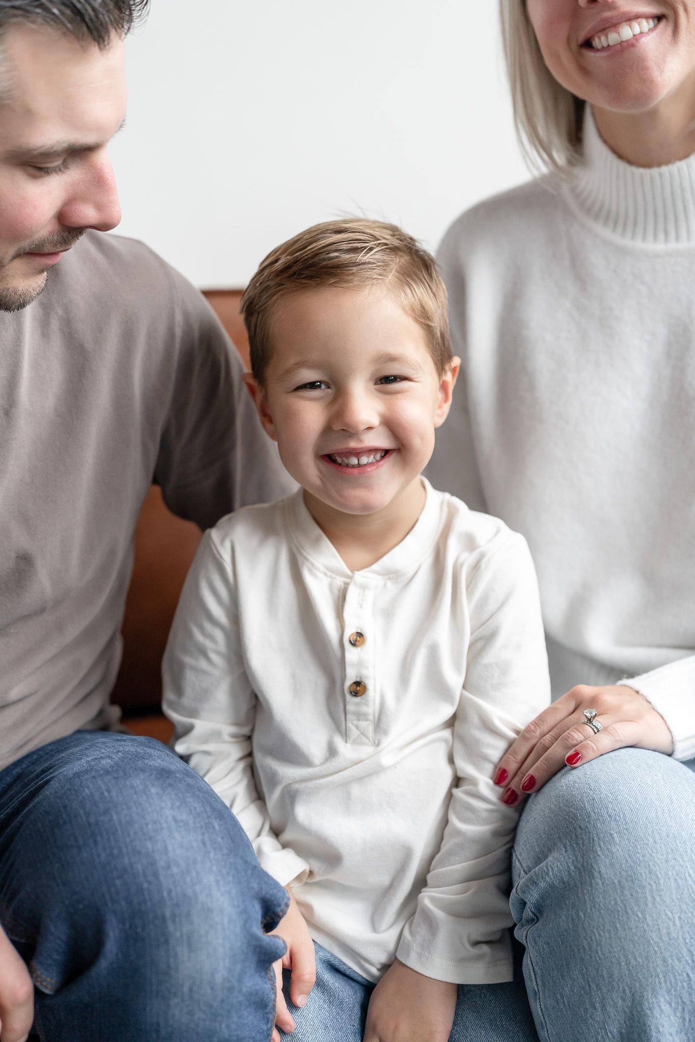 A series of four candid family photos showing joyful moments between parents and child in matching white outfits.