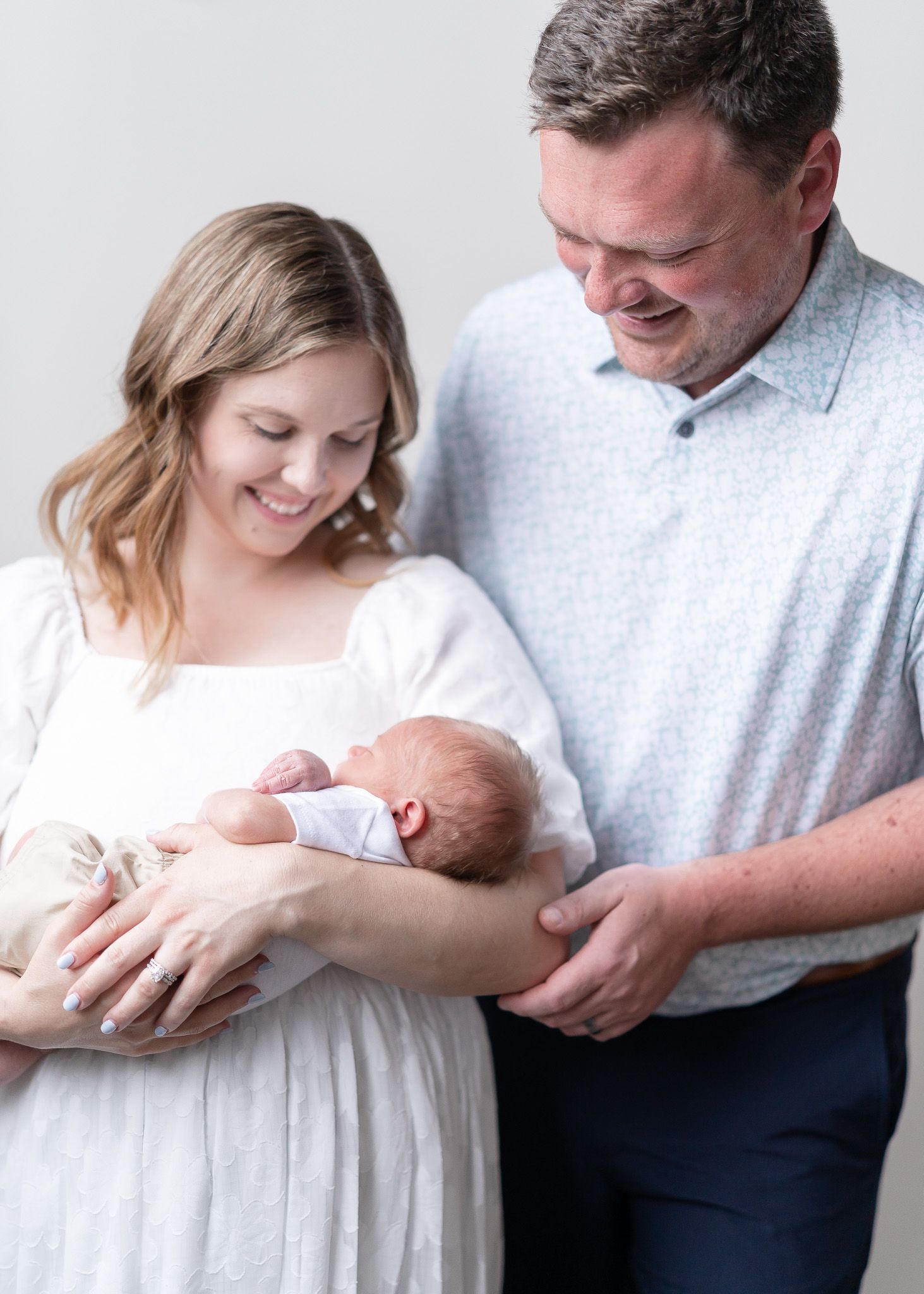 A series of tender moments between parents and their newborn baby in white and gray tones.