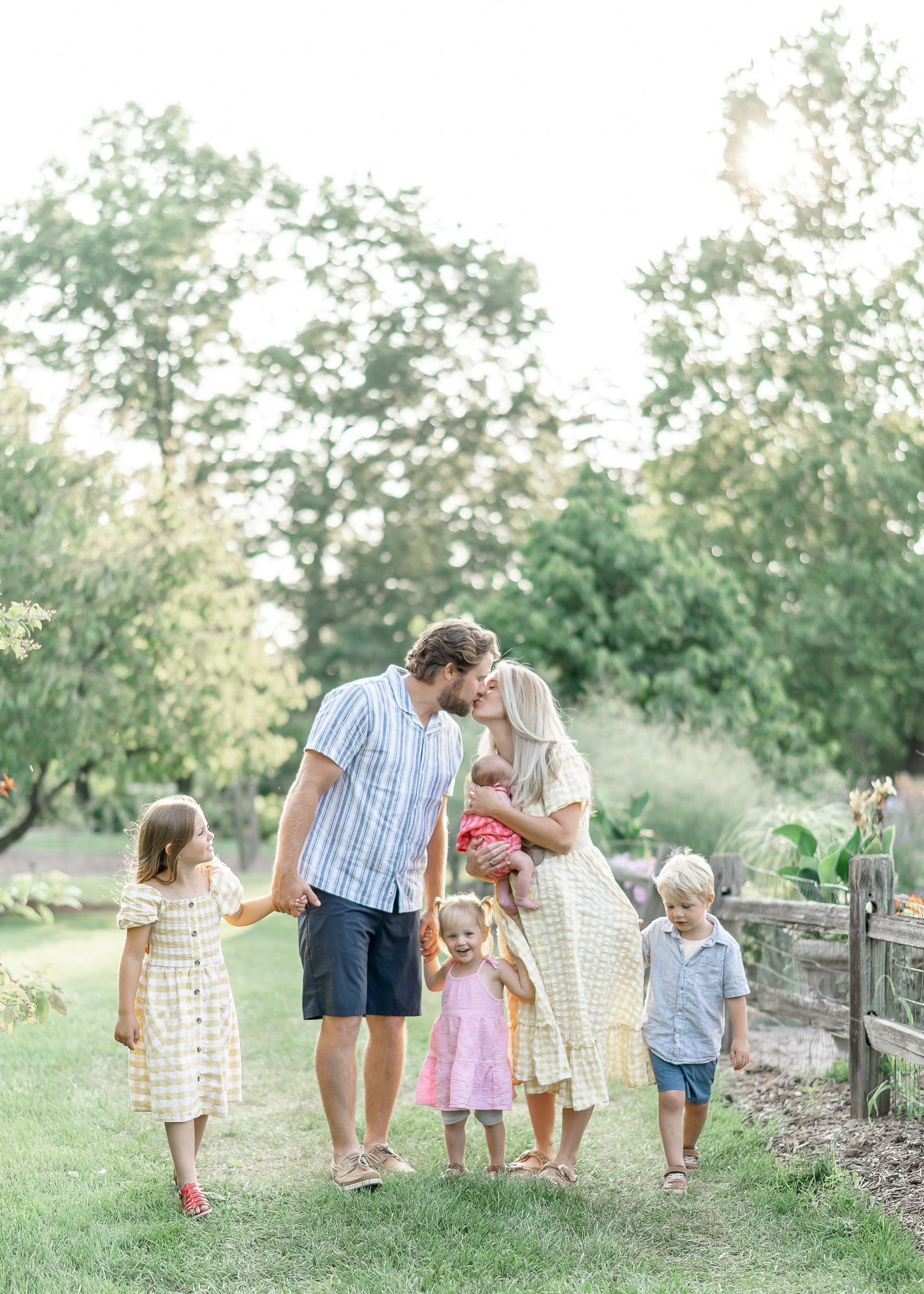 Family walking together along a rustic wooden fence in a lush garden setting during golden hour.