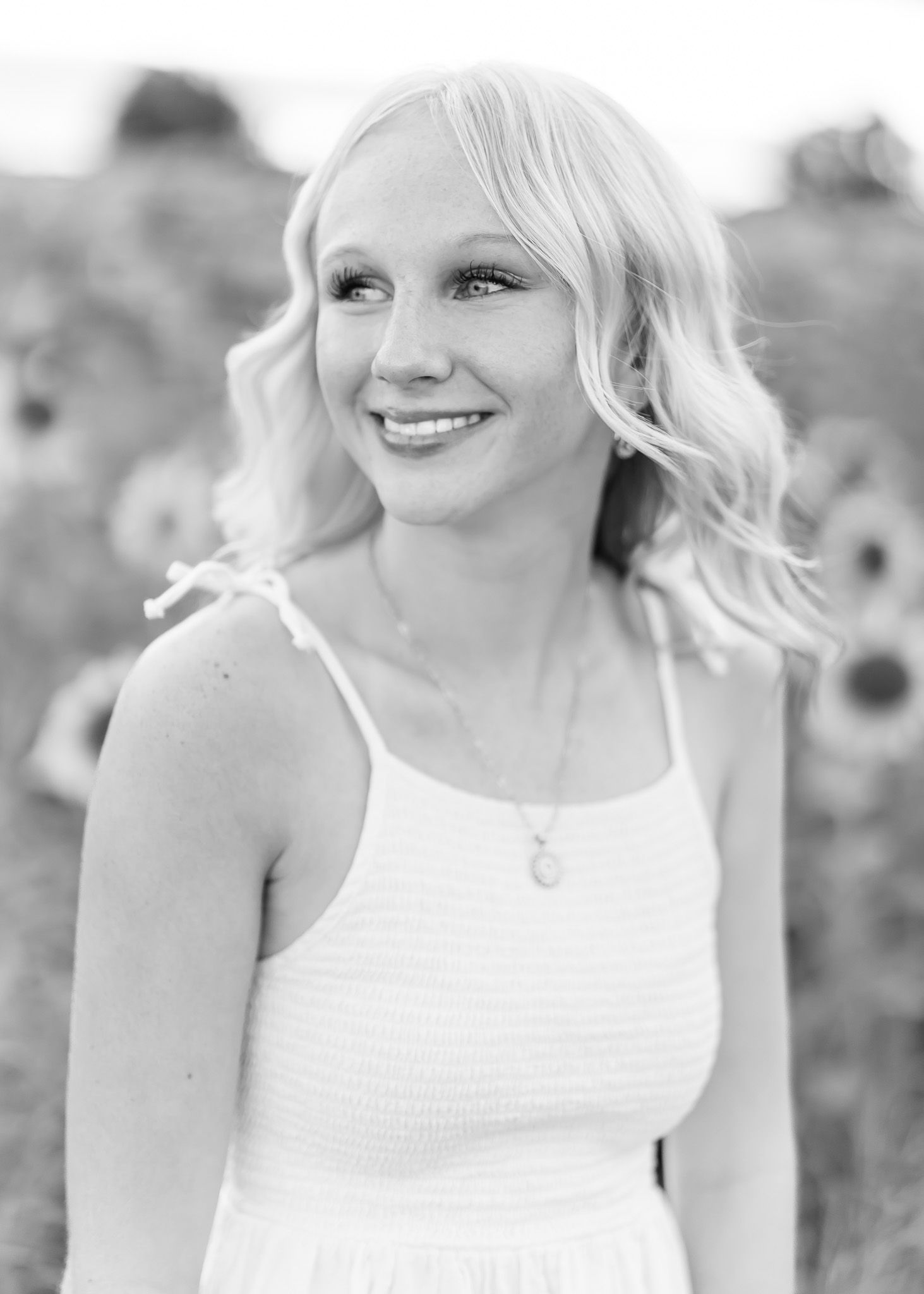 A bride in a white sleeveless dress smiles while posing in a garden setting.