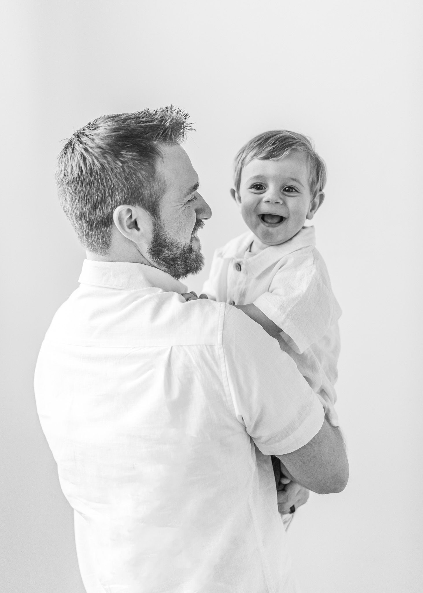 A series of four candid black and white photos showing joyful interactions between an adult and baby against a white backdrop.