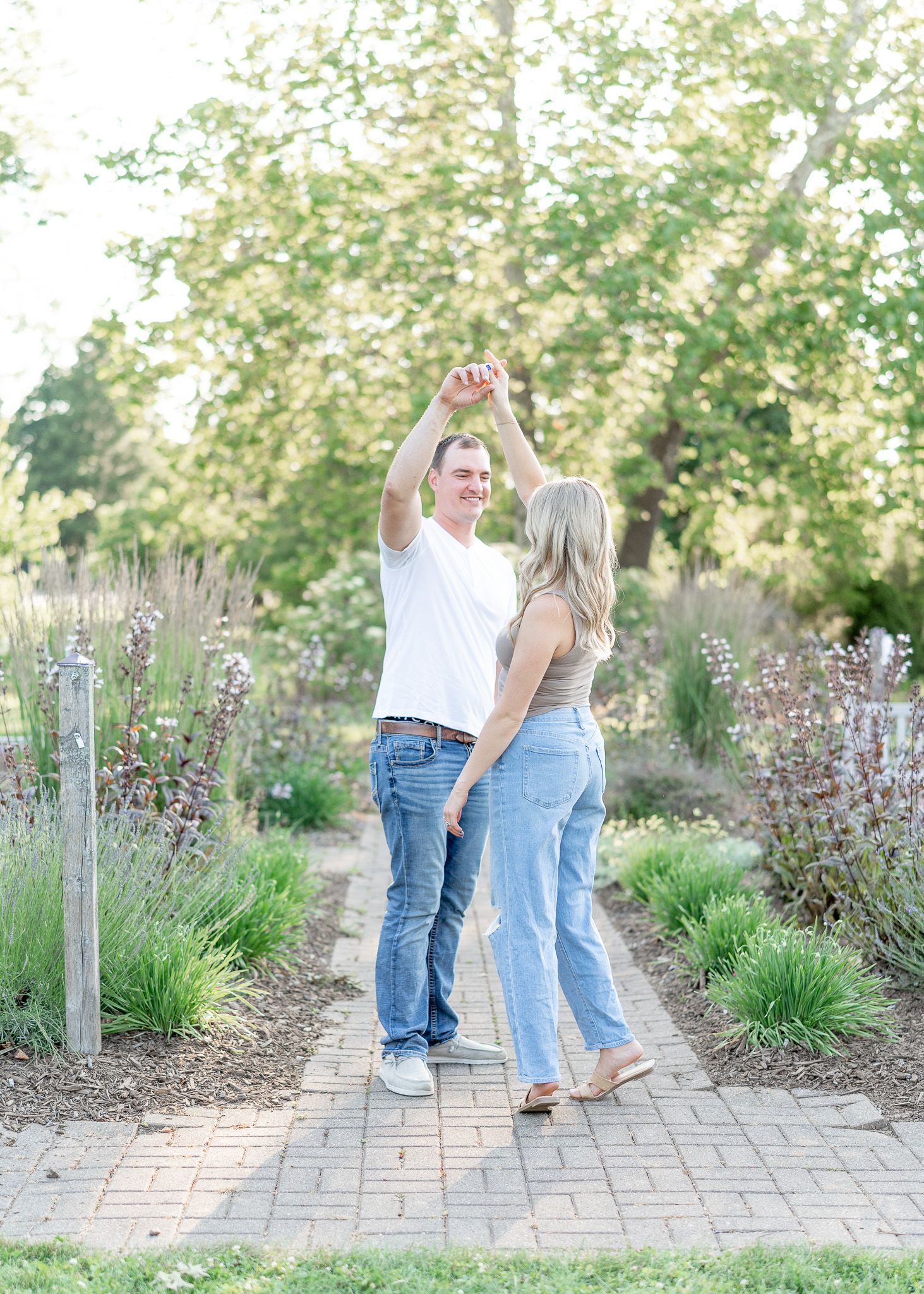 A couple walking along a garden path lined with ornamental grasses and flowering plants on a sunny day.