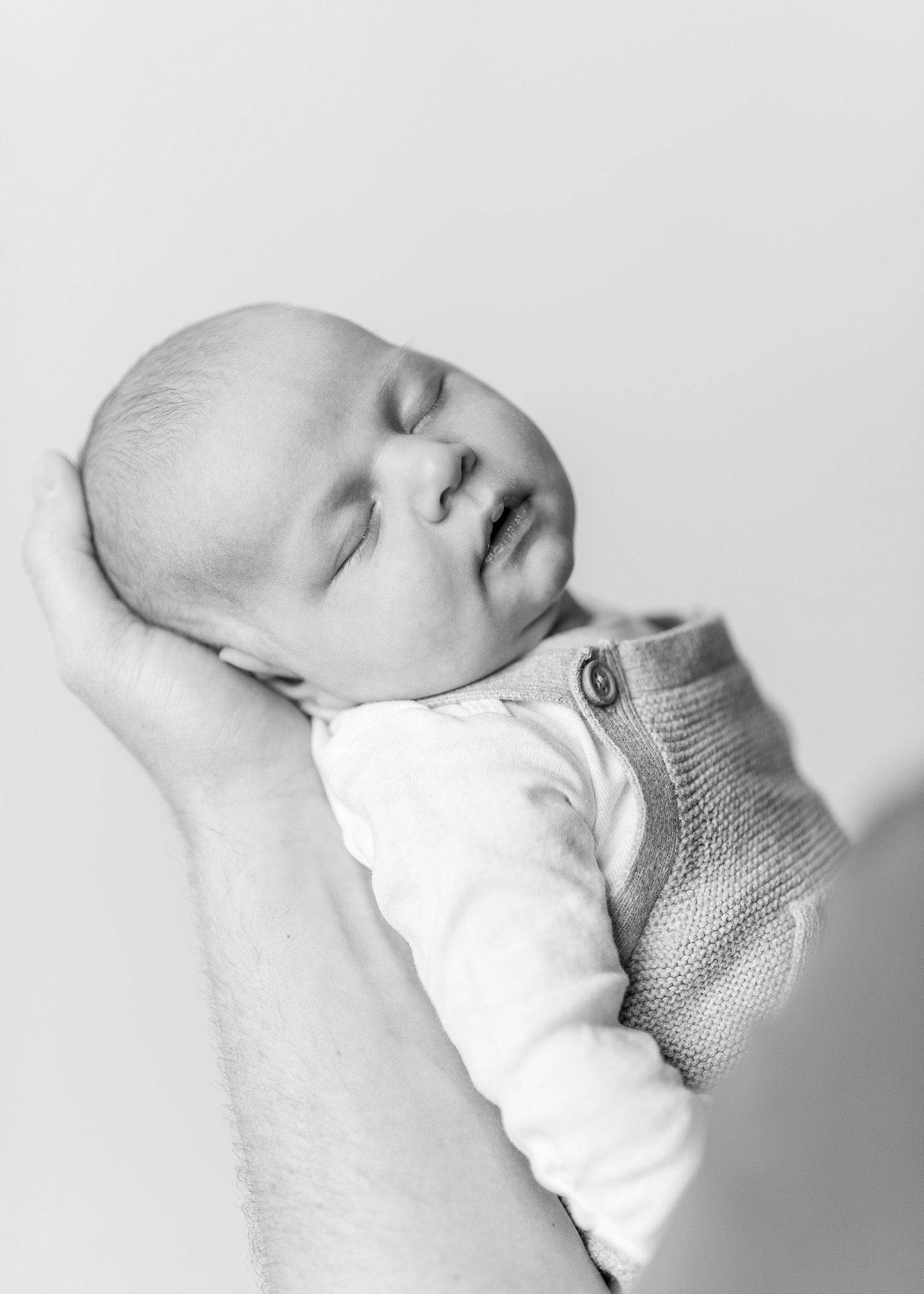 Black and white portrait series showing an infant sleeping peacefully in a cozy knit sweater against a white background.