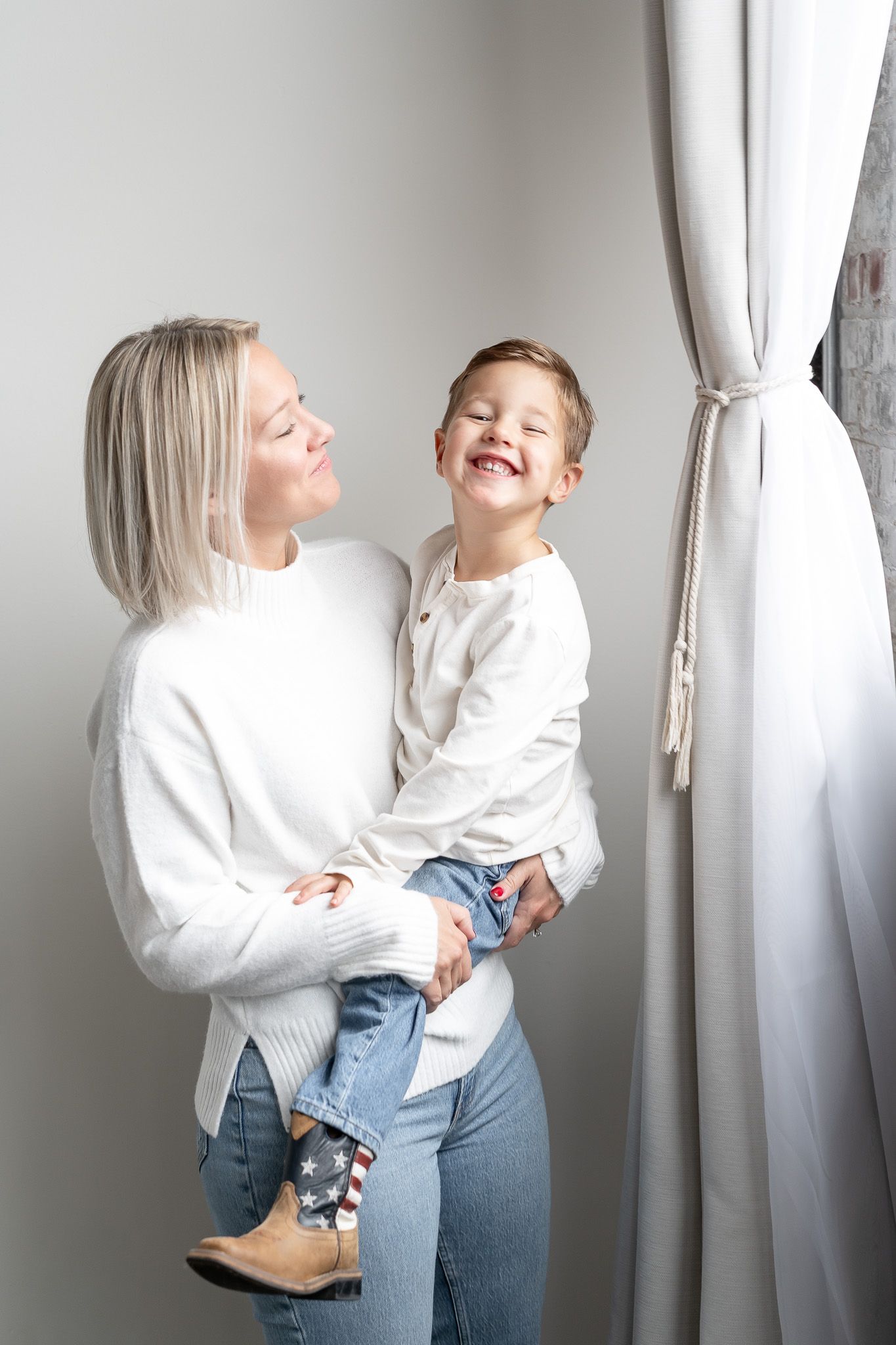 A series of candid photos showing a parent and child in white sweaters sharing joyful moments against a light wall.