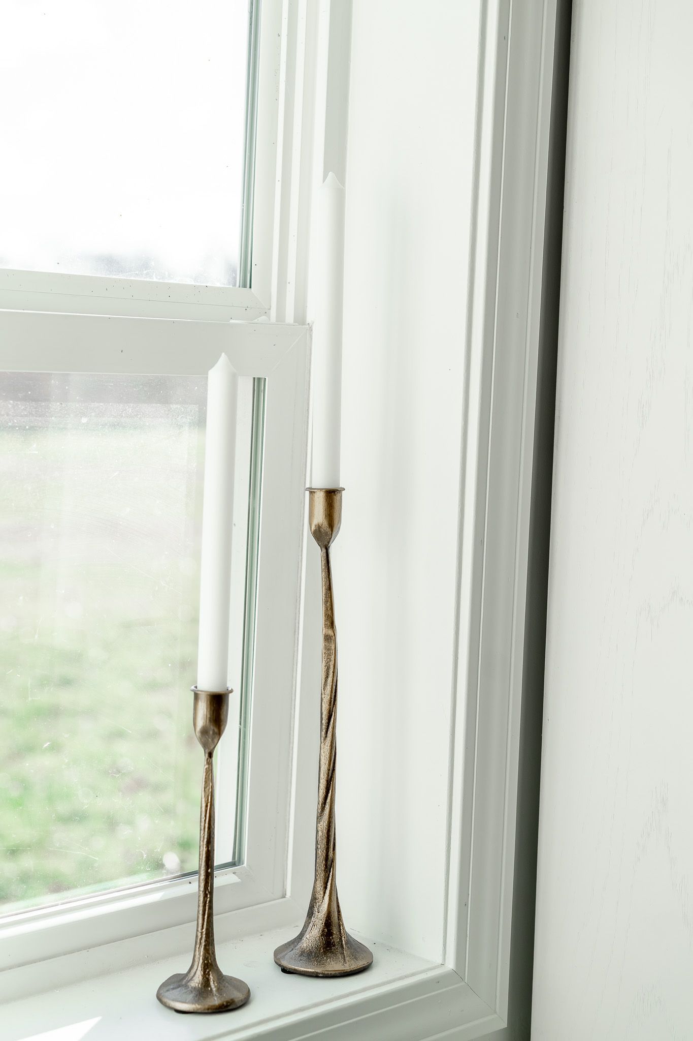 Two elegant brass candlesticks sit on a white windowsill in natural light.