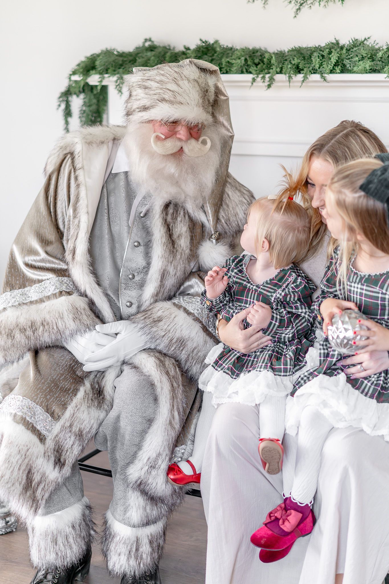 Santa Claus in a gray suit interacts joyfully with children during a Christmas photo session.