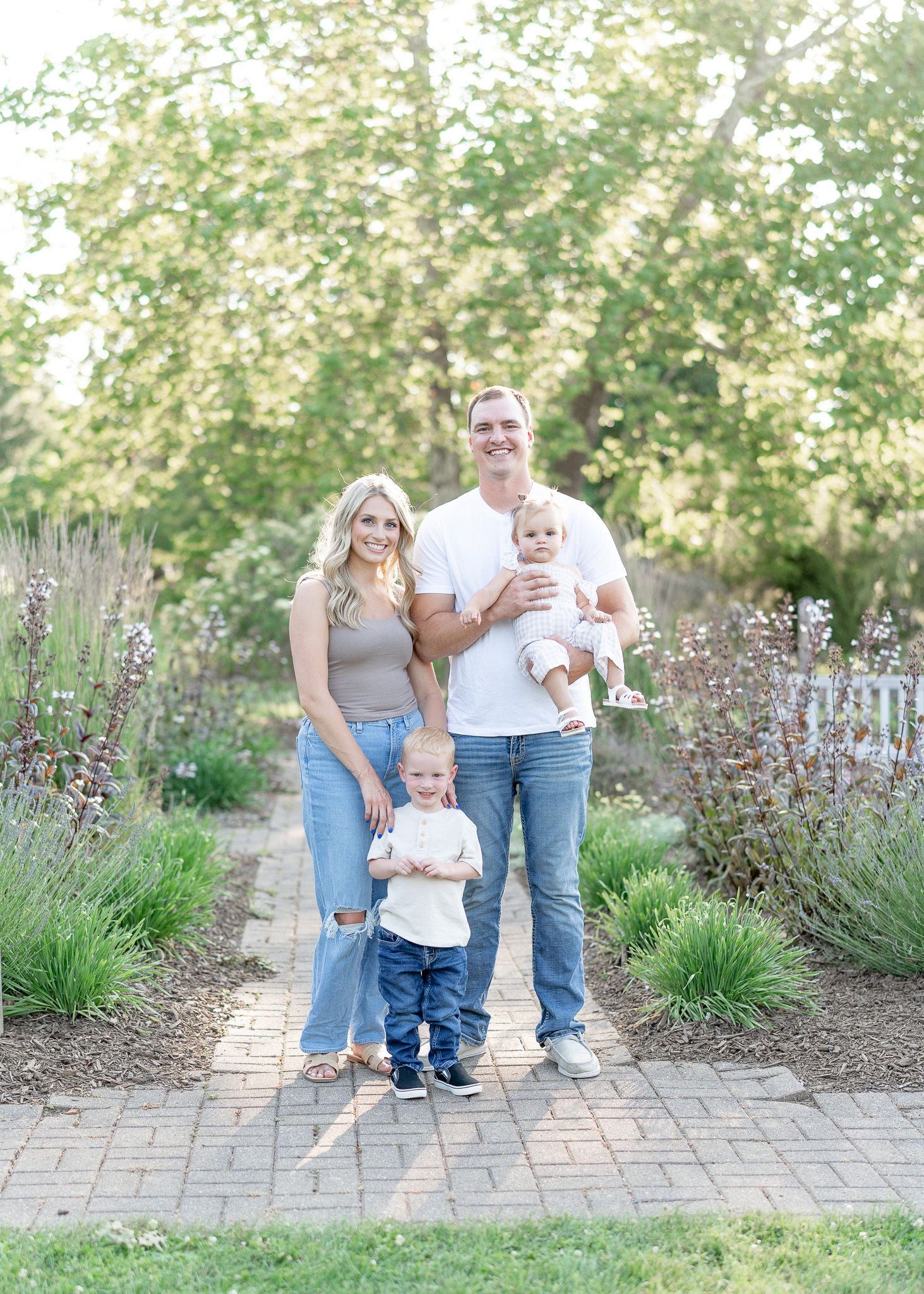 Family poses together on a stone path with lavender plants and greenery in the background.