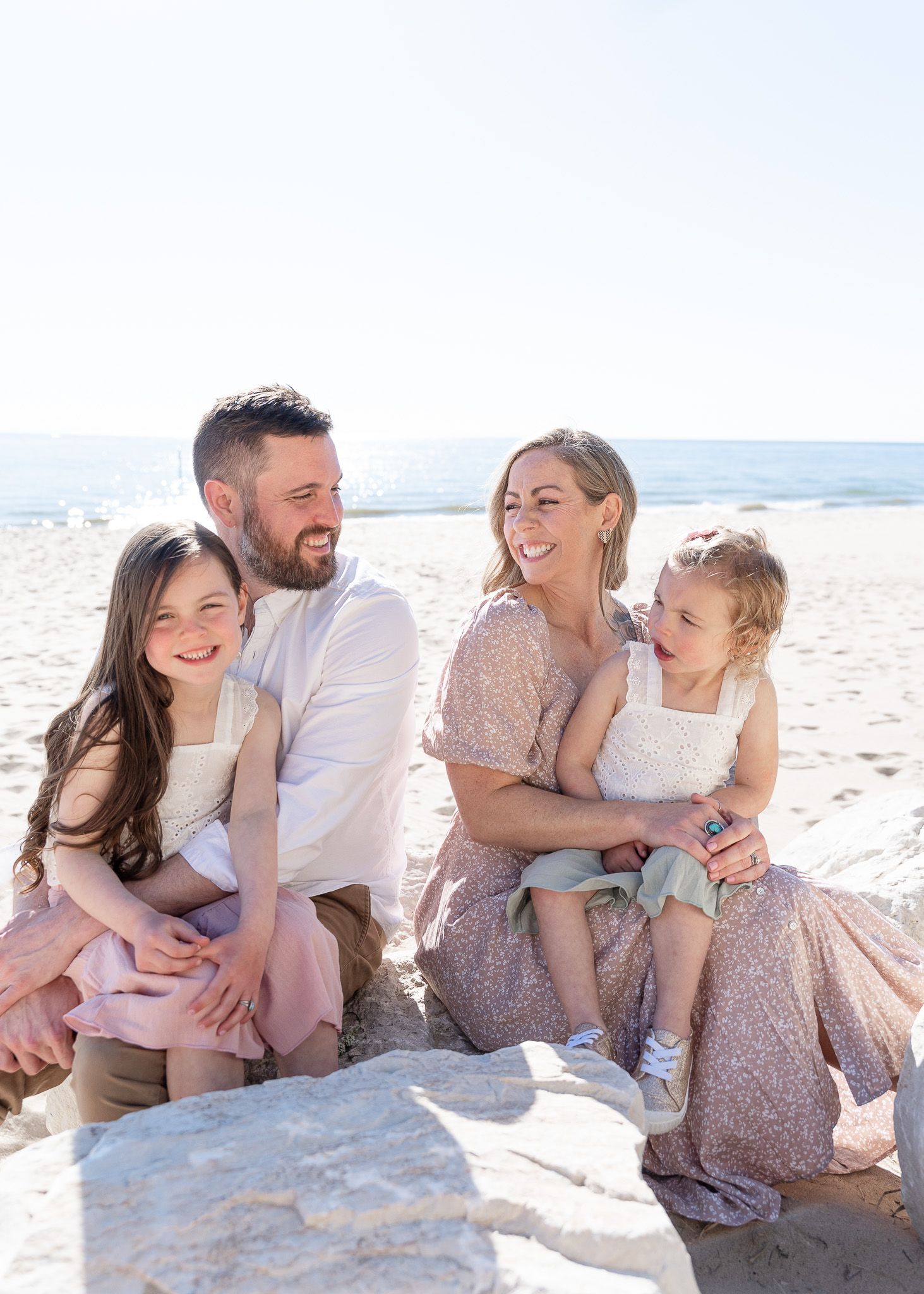 A family shares joyful moments together while sitting on a sandy beach near the ocean on a sunny day.
