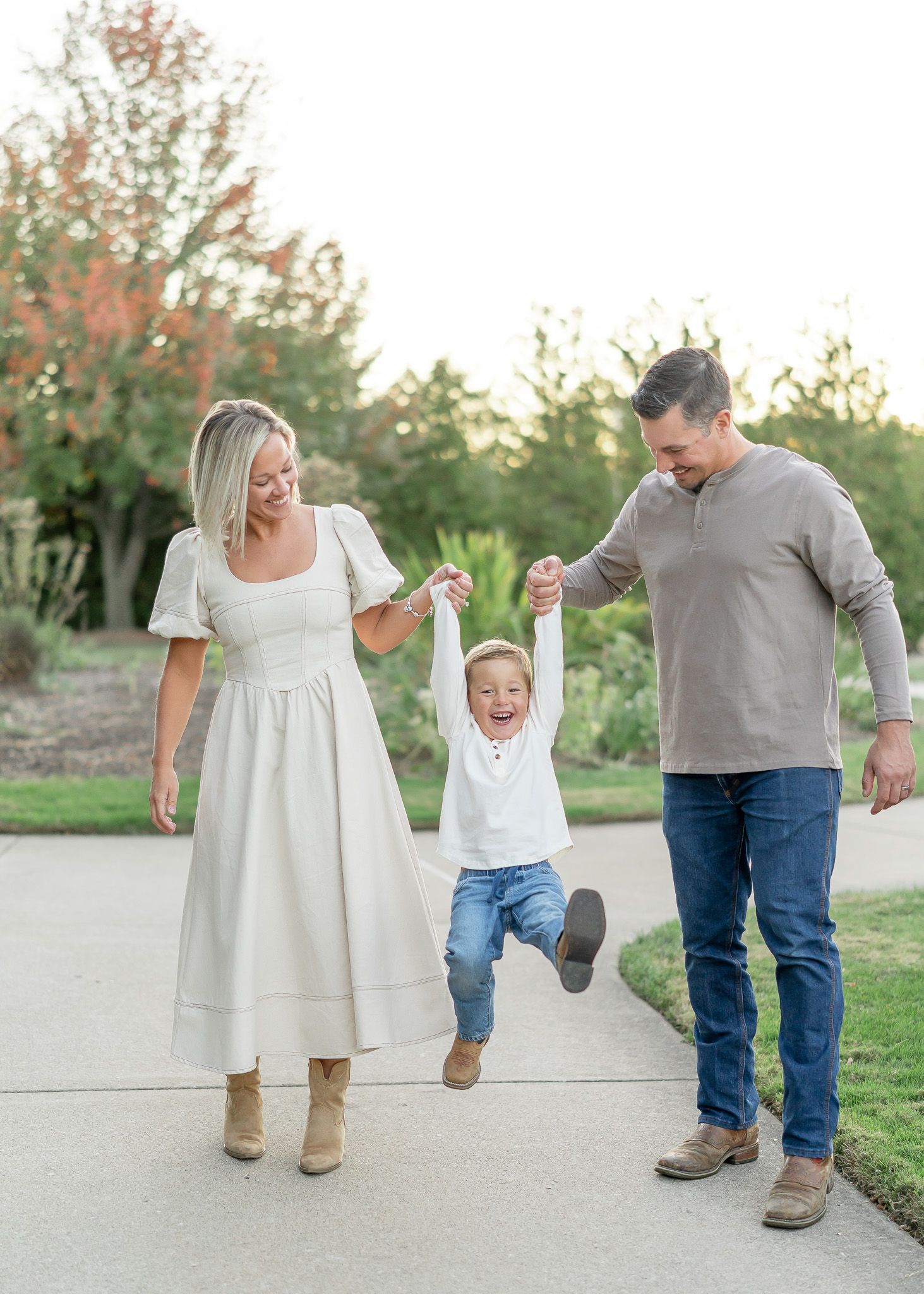 Family walking together outdoors holding hands and playfully swinging child between them at sunset.