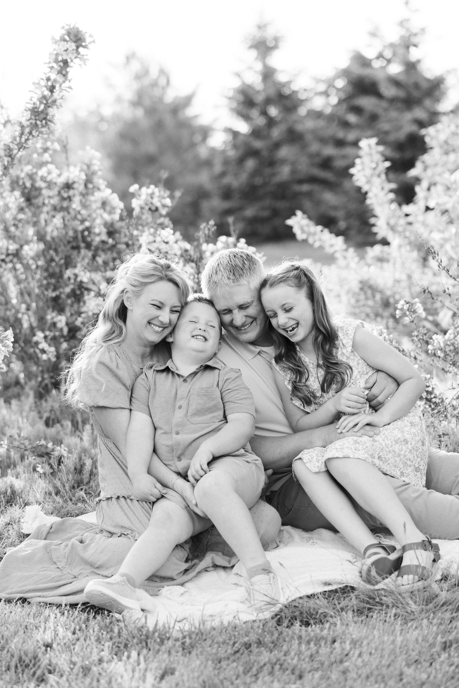 A family sits together on a blanket outdoors surrounded by blooming flowers in a black and white photograph.