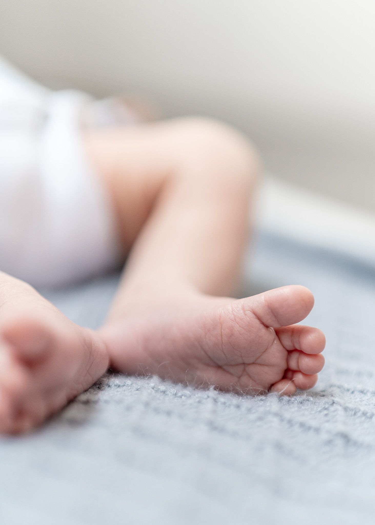 Close-up view of tiny baby feet resting on soft gray textured fabric creating a tender newborn photography scene.