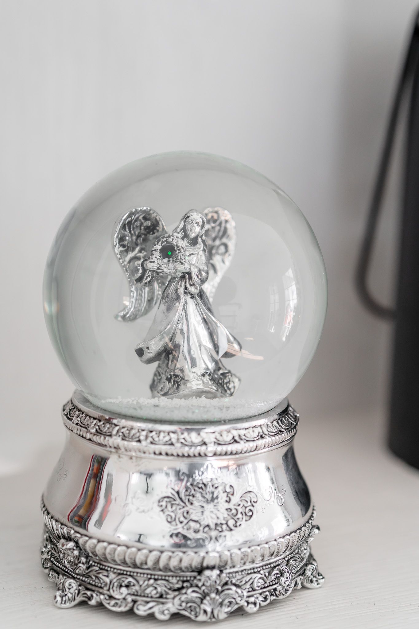 An ornate silver snow globe featuring an angel figure on an intricate metallic base.