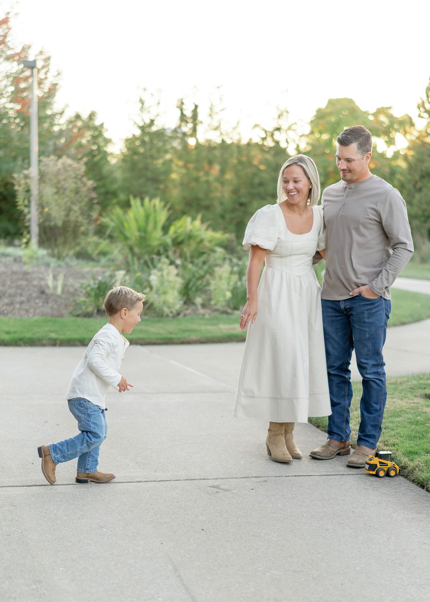 A family in casual attire walks and plays together on a paved path during golden hour at sunset.