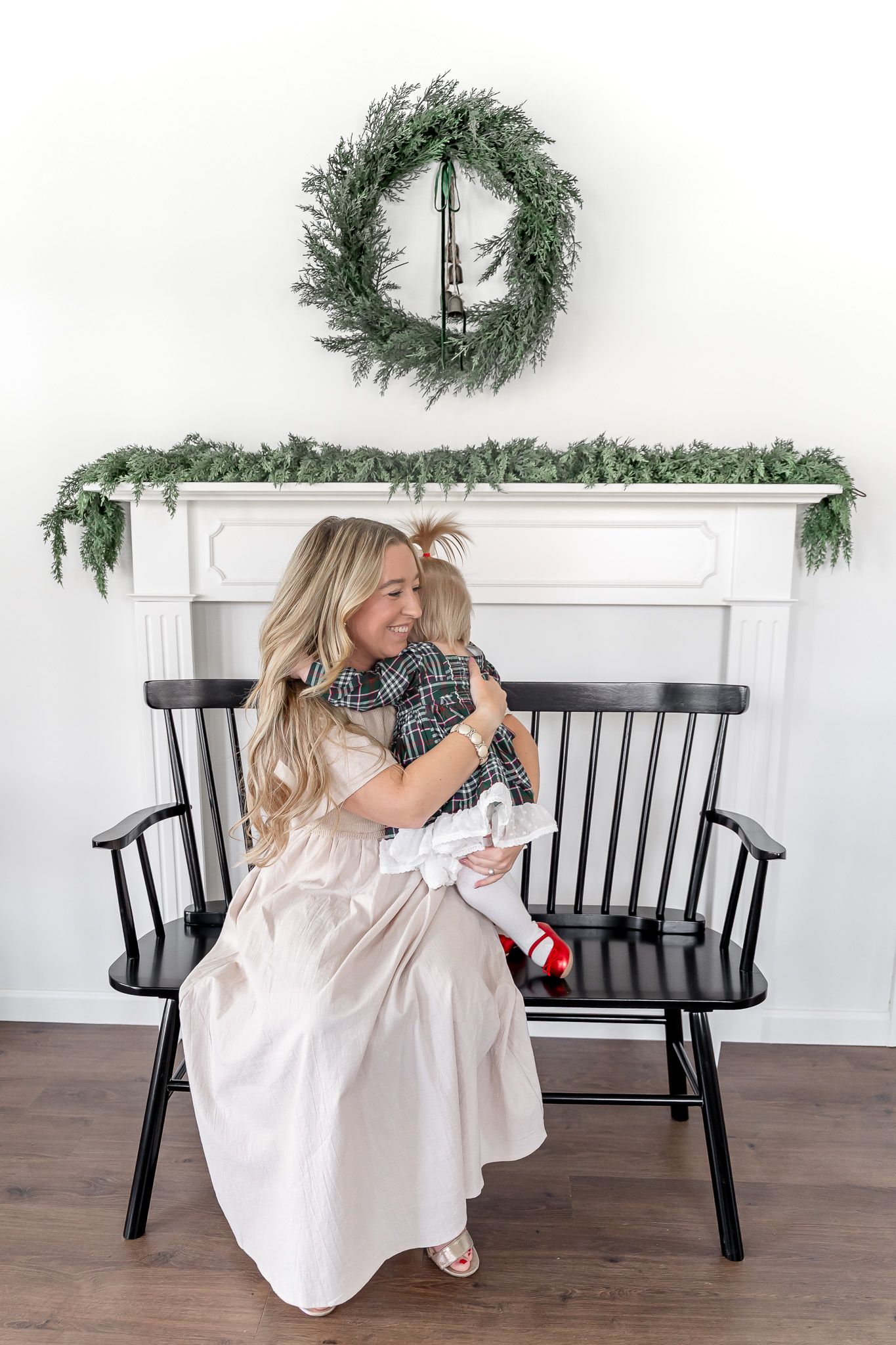 Family sits together on black wooden bench decorated with evergreen holiday wreaths and garland.