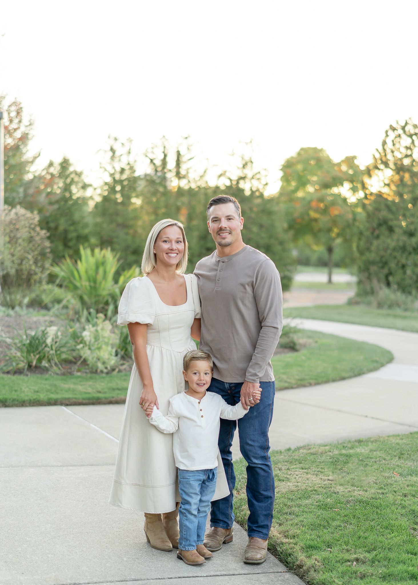 A family in coordinating cream and grey outfits poses together on a winding path during golden hour.