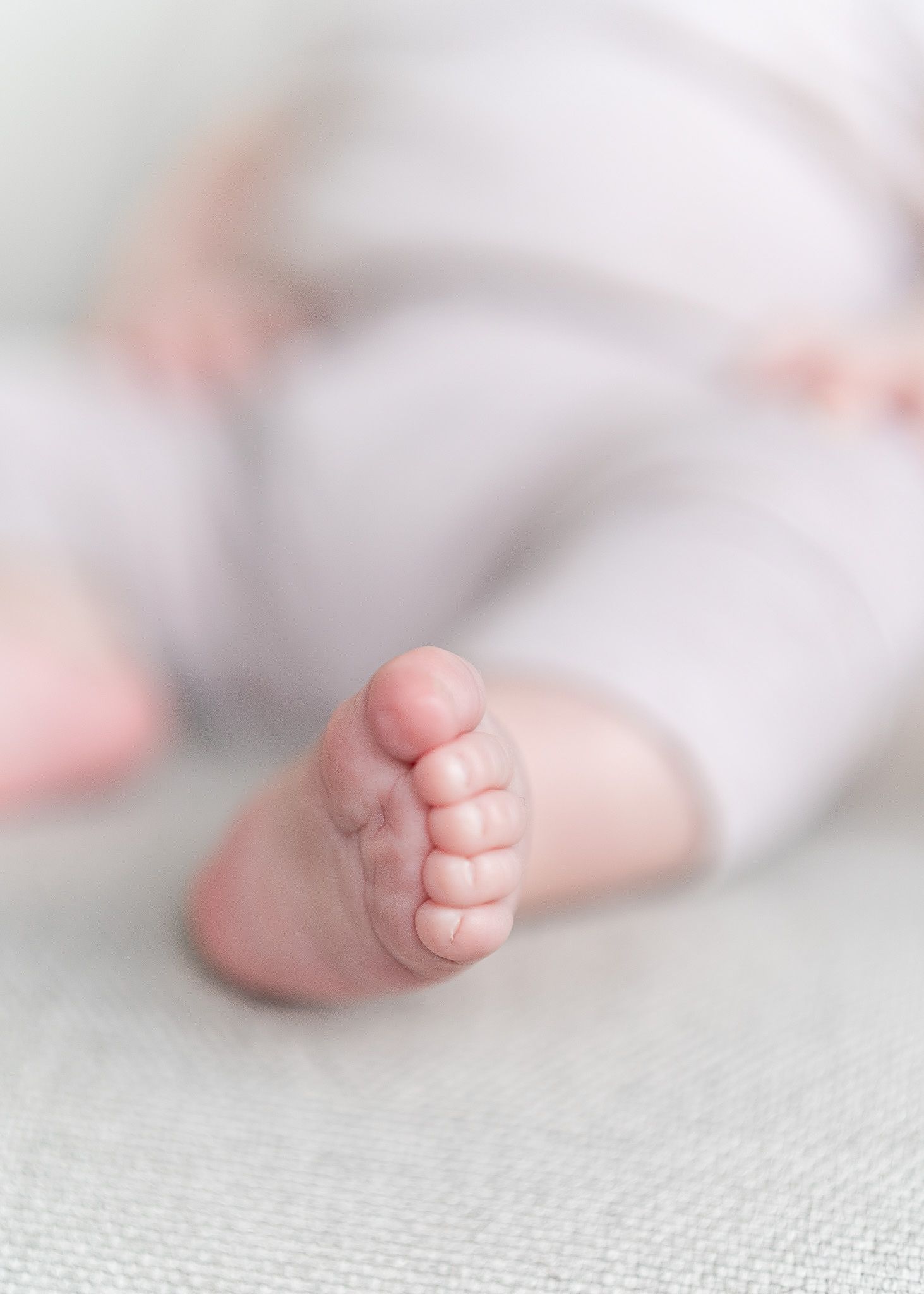 Close-up photo of a tiny baby's foot resting on soft white textured fabric with a gentle blur effect.
