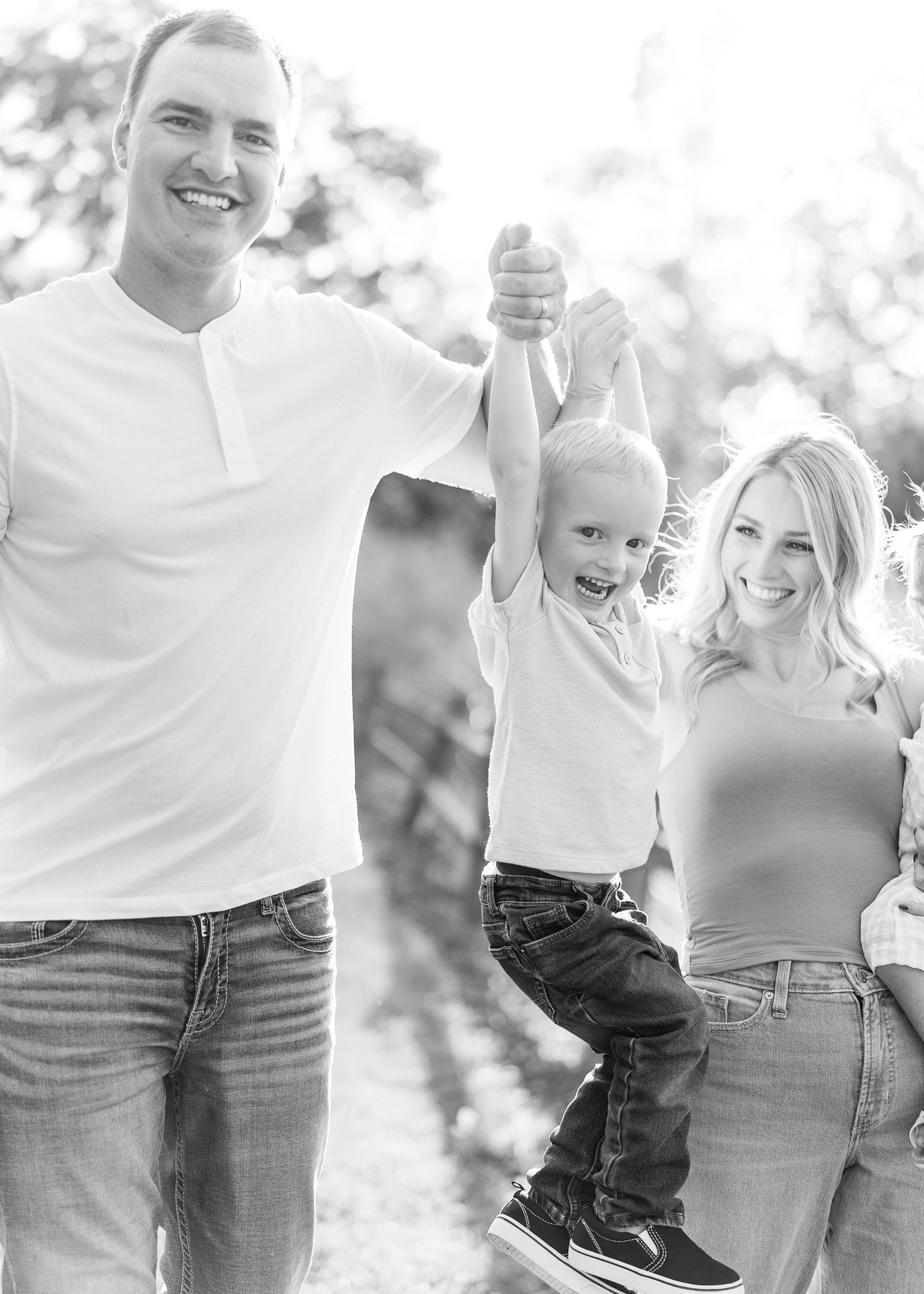 A family wearing white tops and jeans poses together outdoors in a casual photo session.