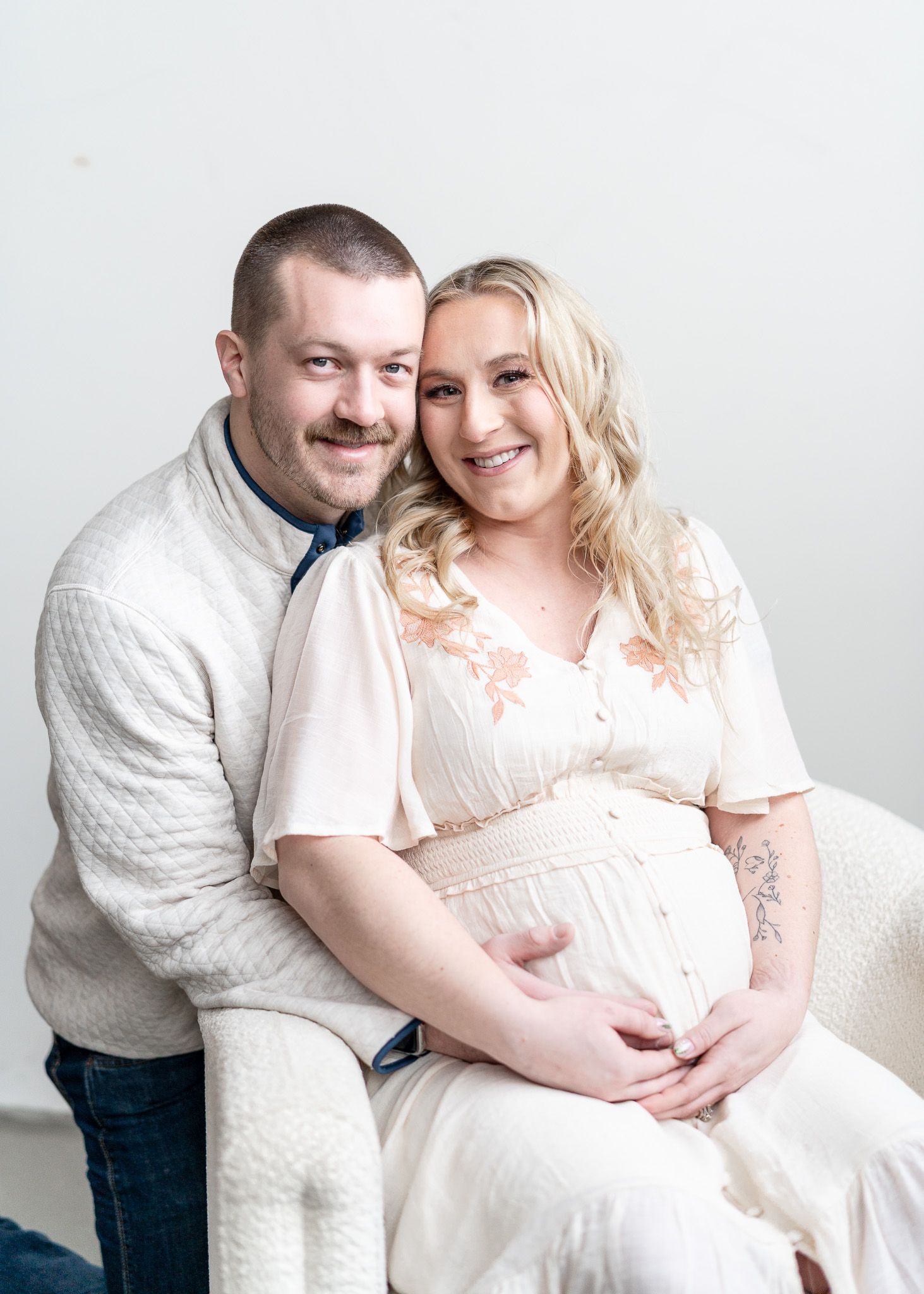 Maternity photo series showing couple in white and denim embracing against white background.