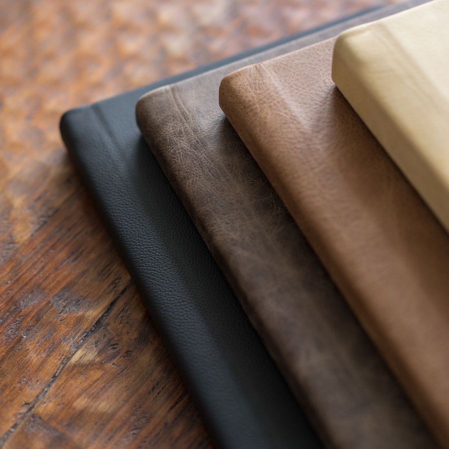 A series of leather swatches in black, brown, and beige arranged in a gradient pattern on a wooden surface.