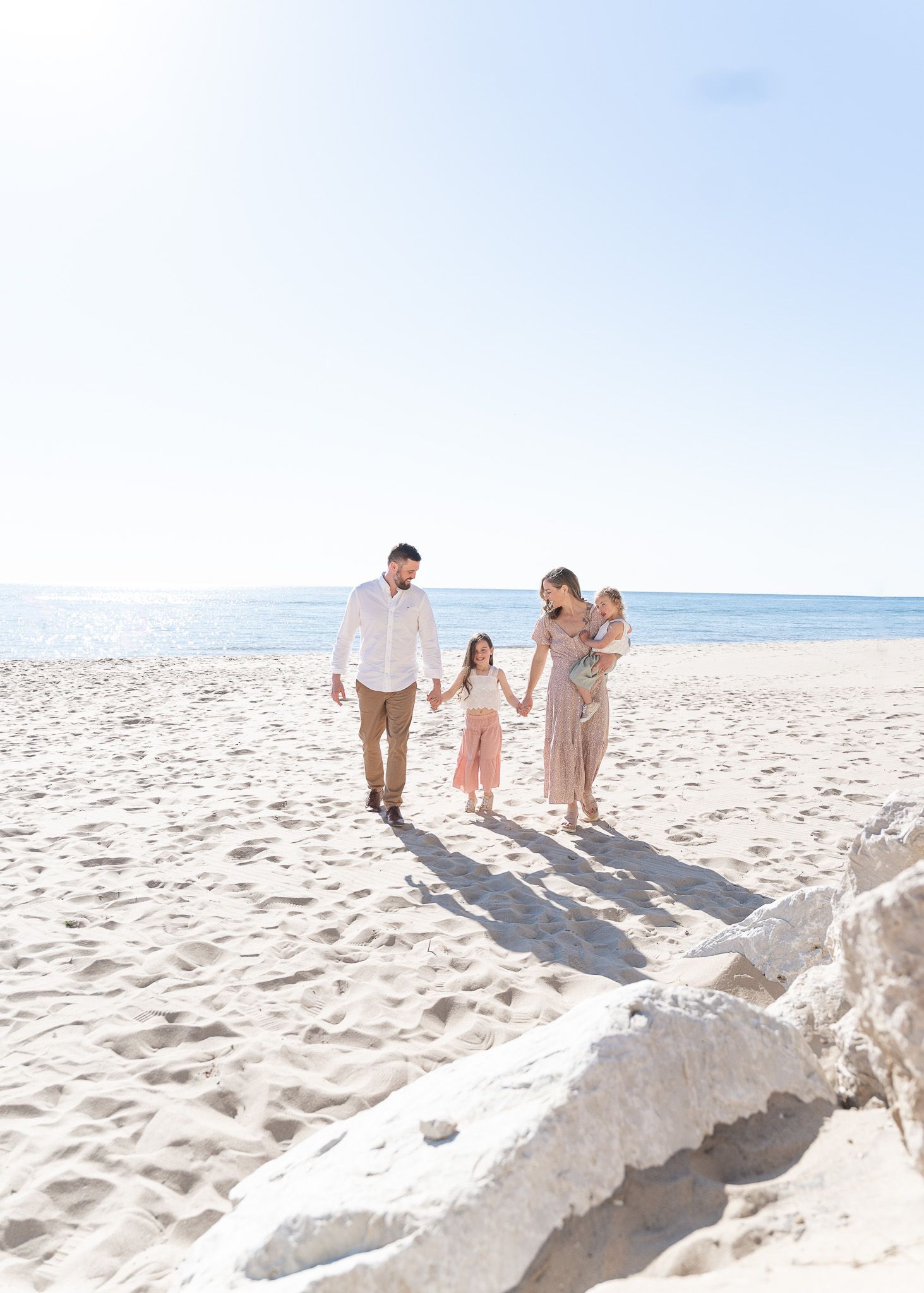 Family walking together on a sunny beach with a large sand castle in the foreground.