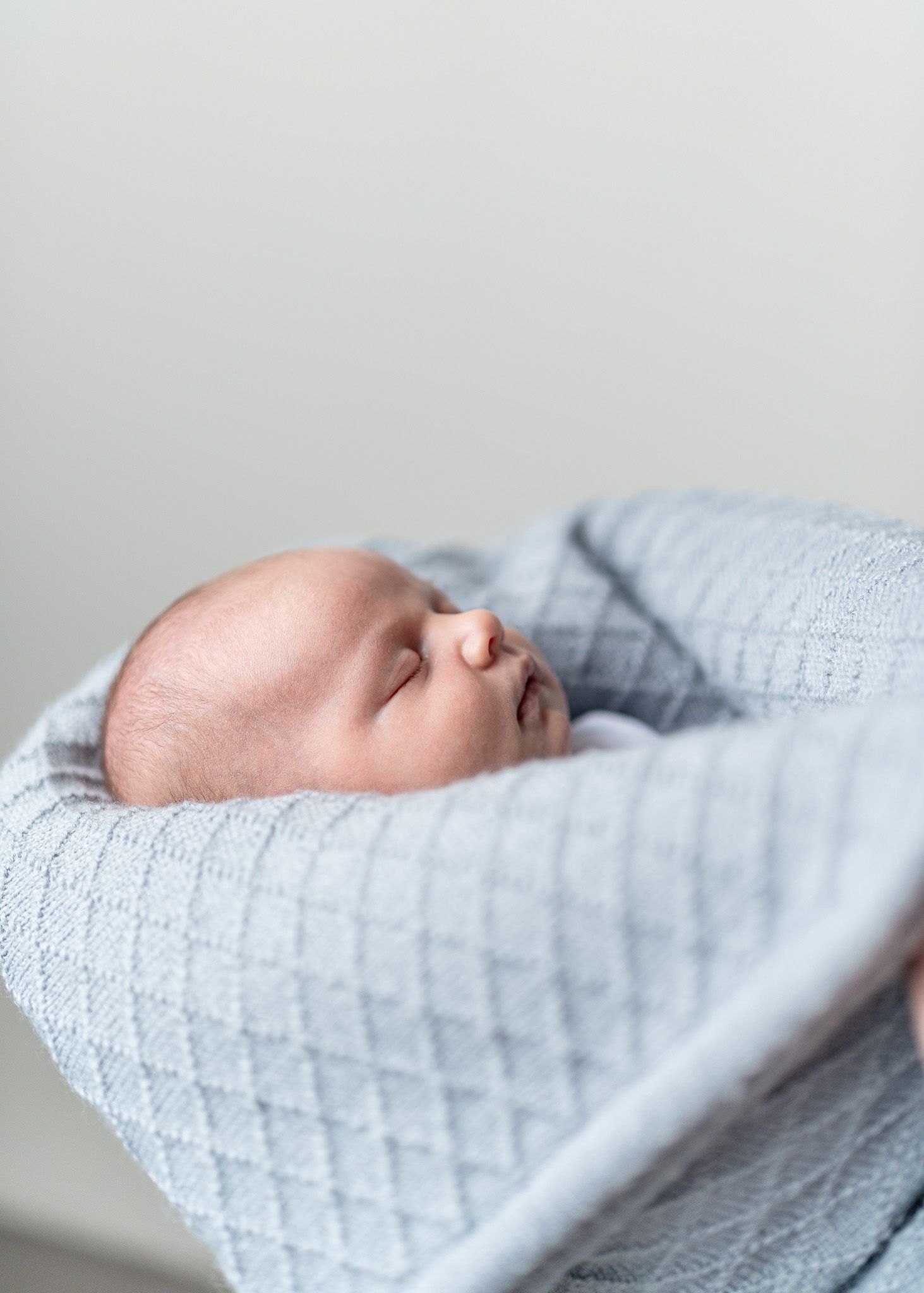 Sleeping newborn baby wrapped in textured light blue blanket against white background.
