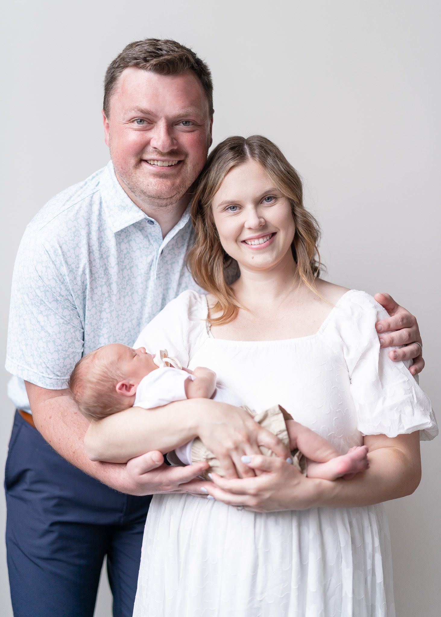 A series of four studio portraits showing a couple in white and navy clothing holding a newborn baby against a light backdrop.