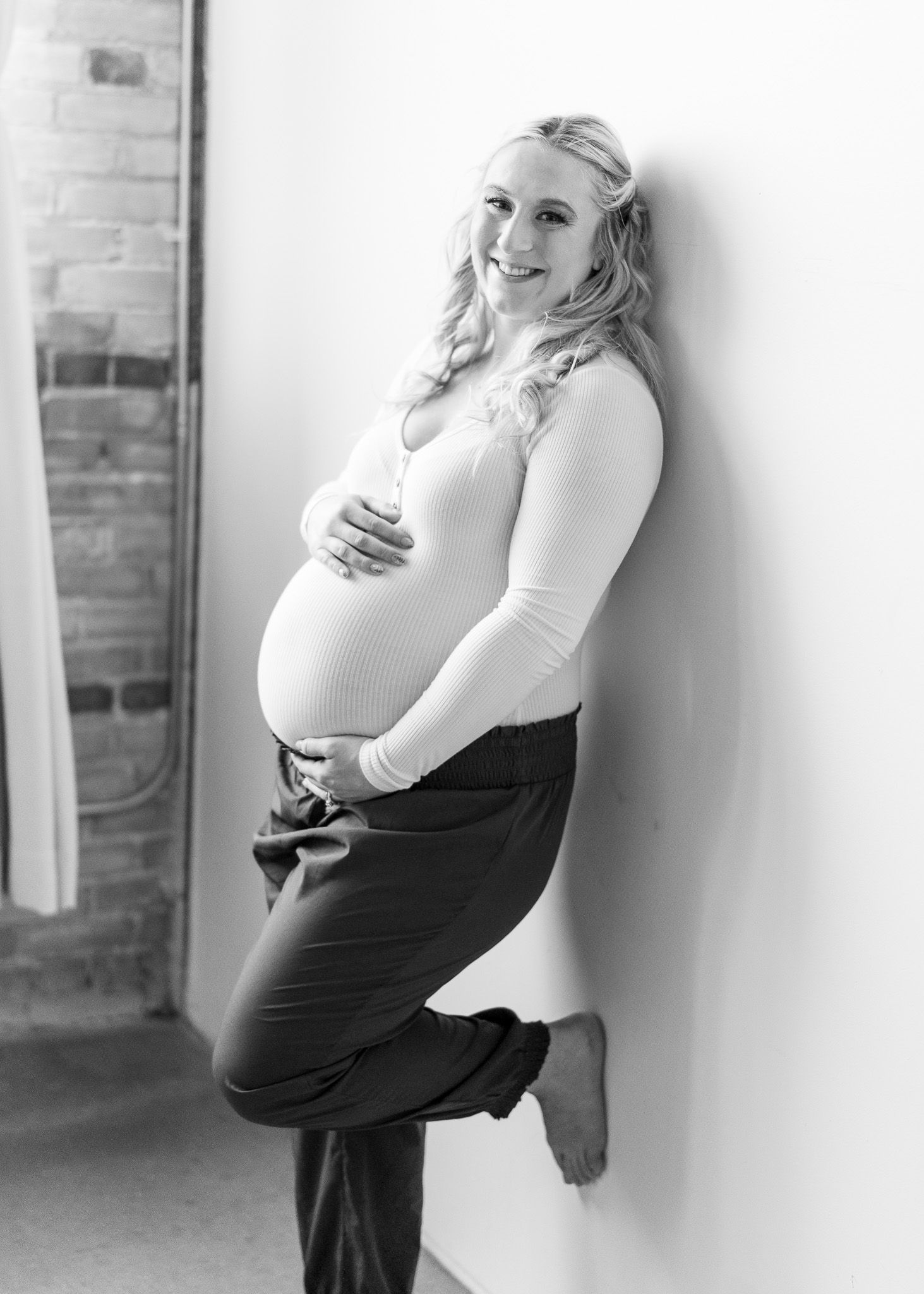 Black and white maternity photo series showing a pregnant woman in a white top and black skirt against a wall.