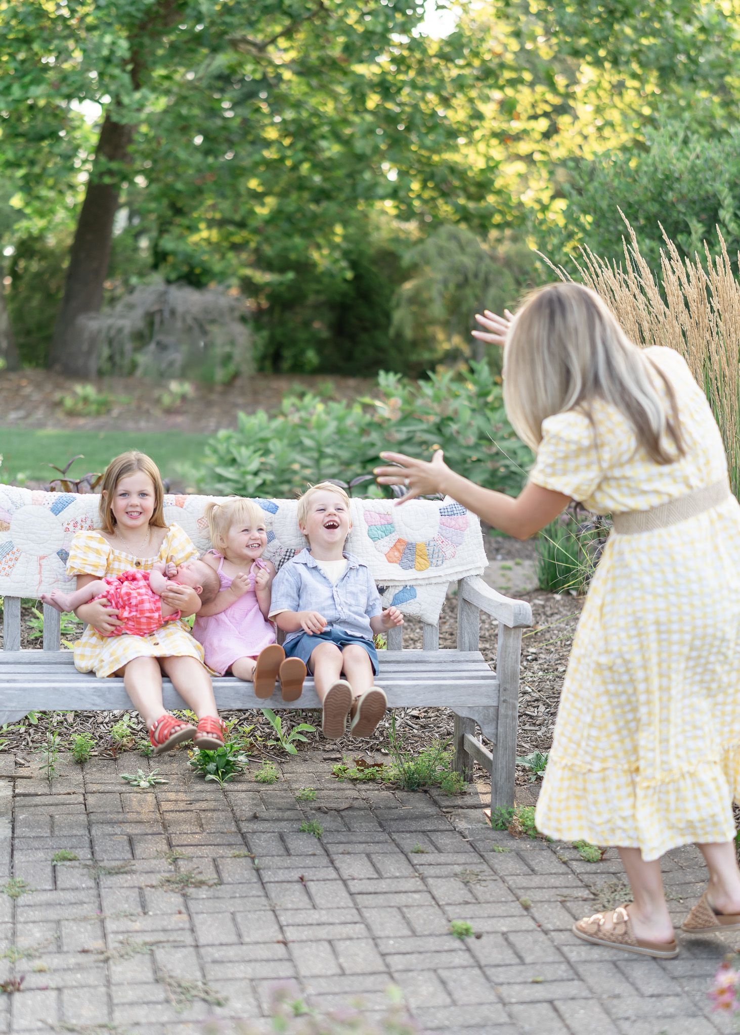 Children playing and laughing together on a stone bench in a garden setting during a sunny day.