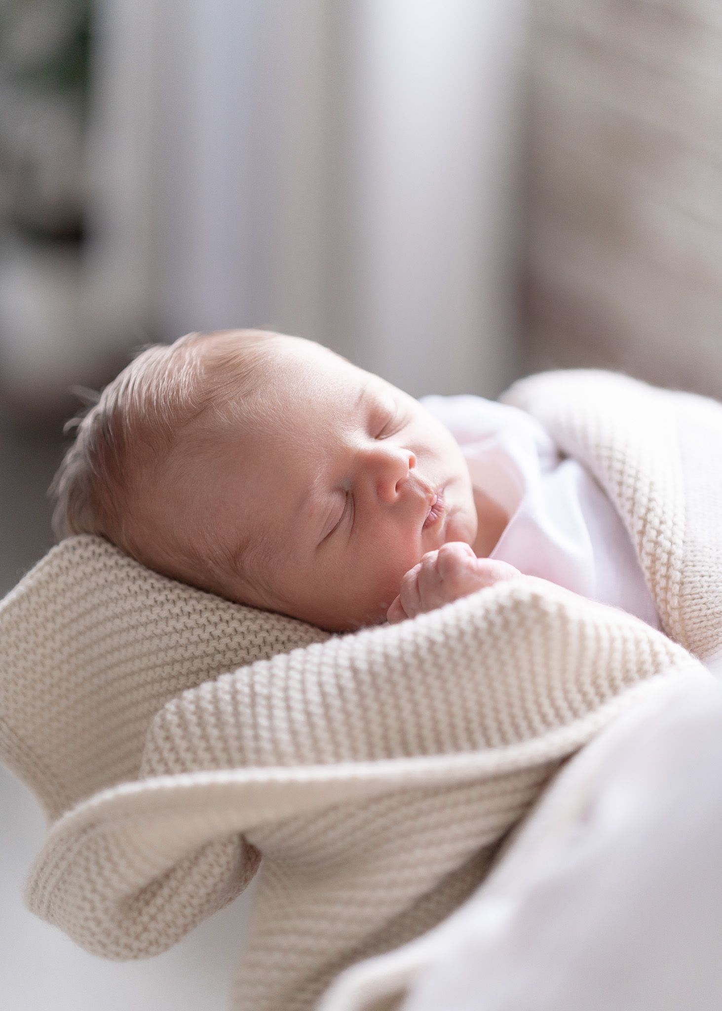 A peaceful newborn baby sleeps soundly while wrapped in a soft white knitted blanket.