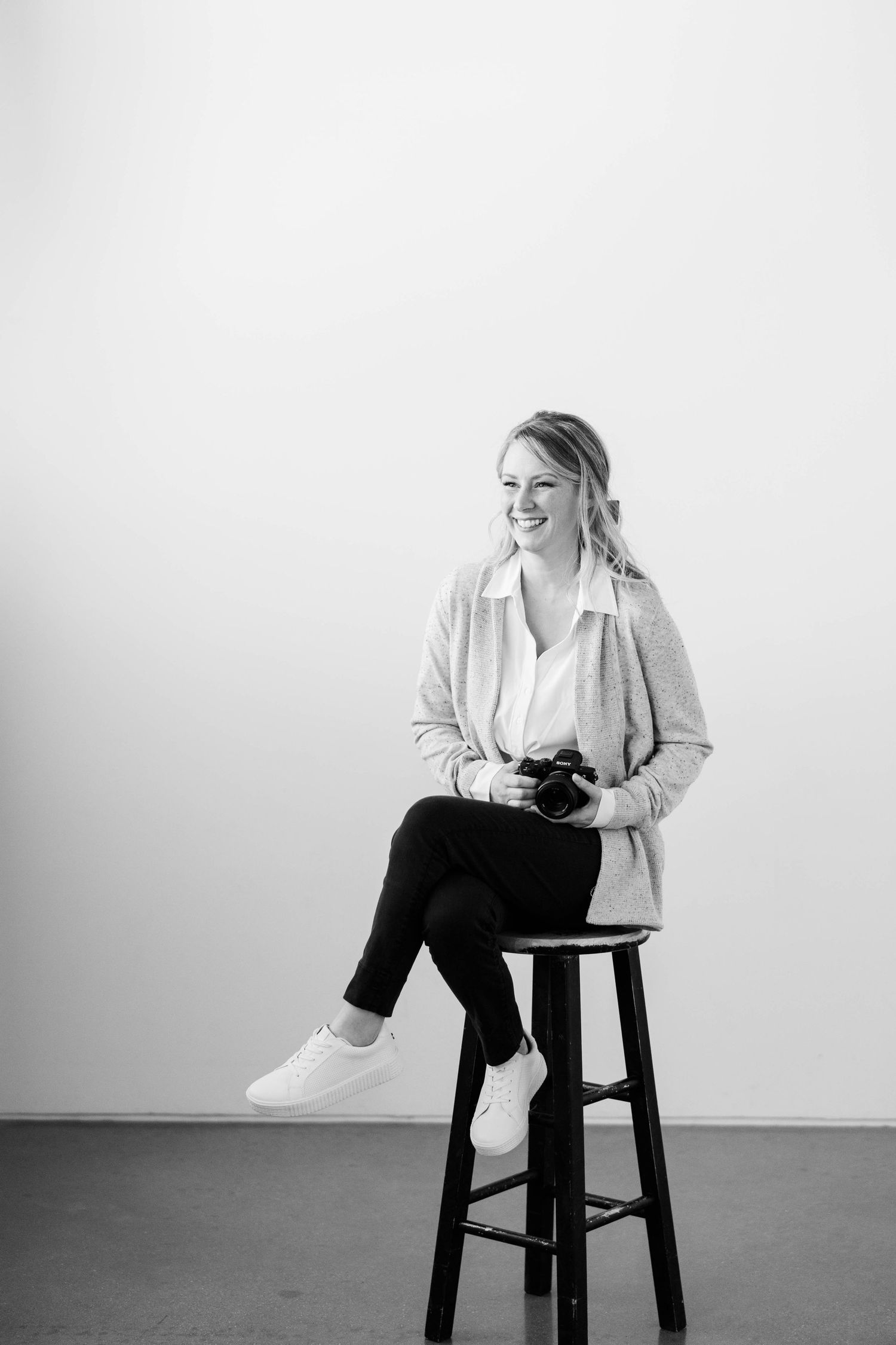 Professional studio portraits in black and white show a seated figure in white blazer and dark pants on a stool.