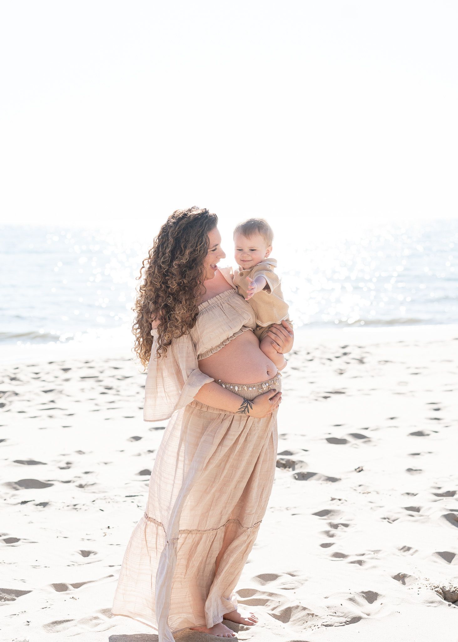 Family in light-colored outfits walking along a sandy beach with ocean waves in the background.