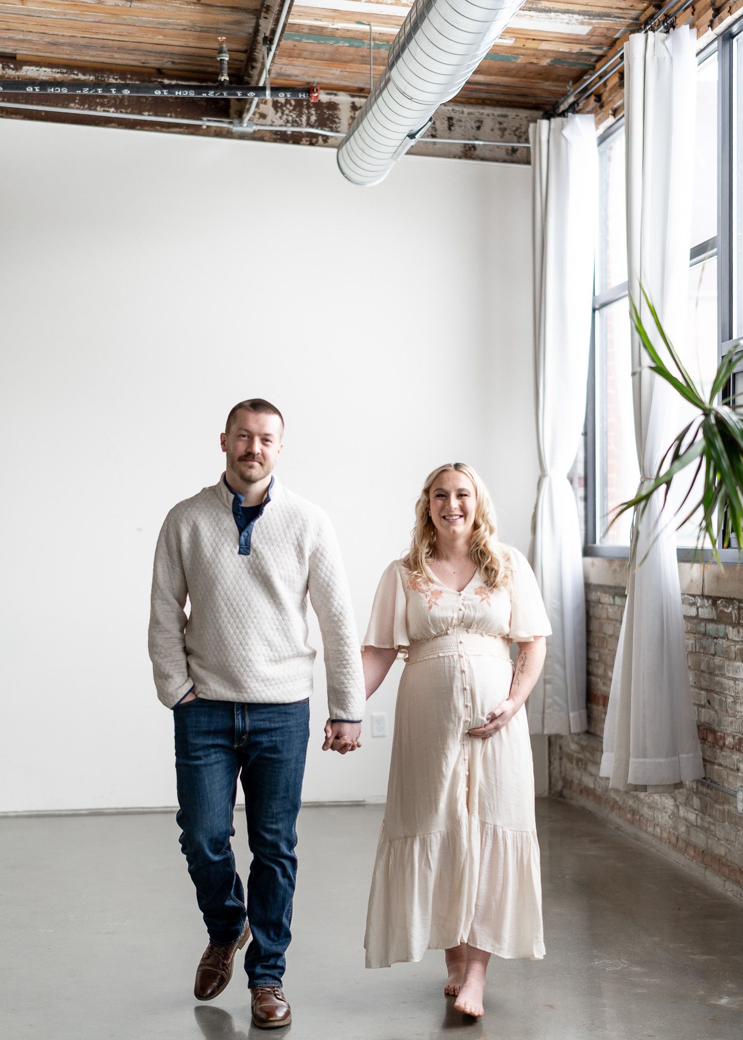 A couple in coordinated outfits walks through a bright industrial space with exposed brick walls and white decor.