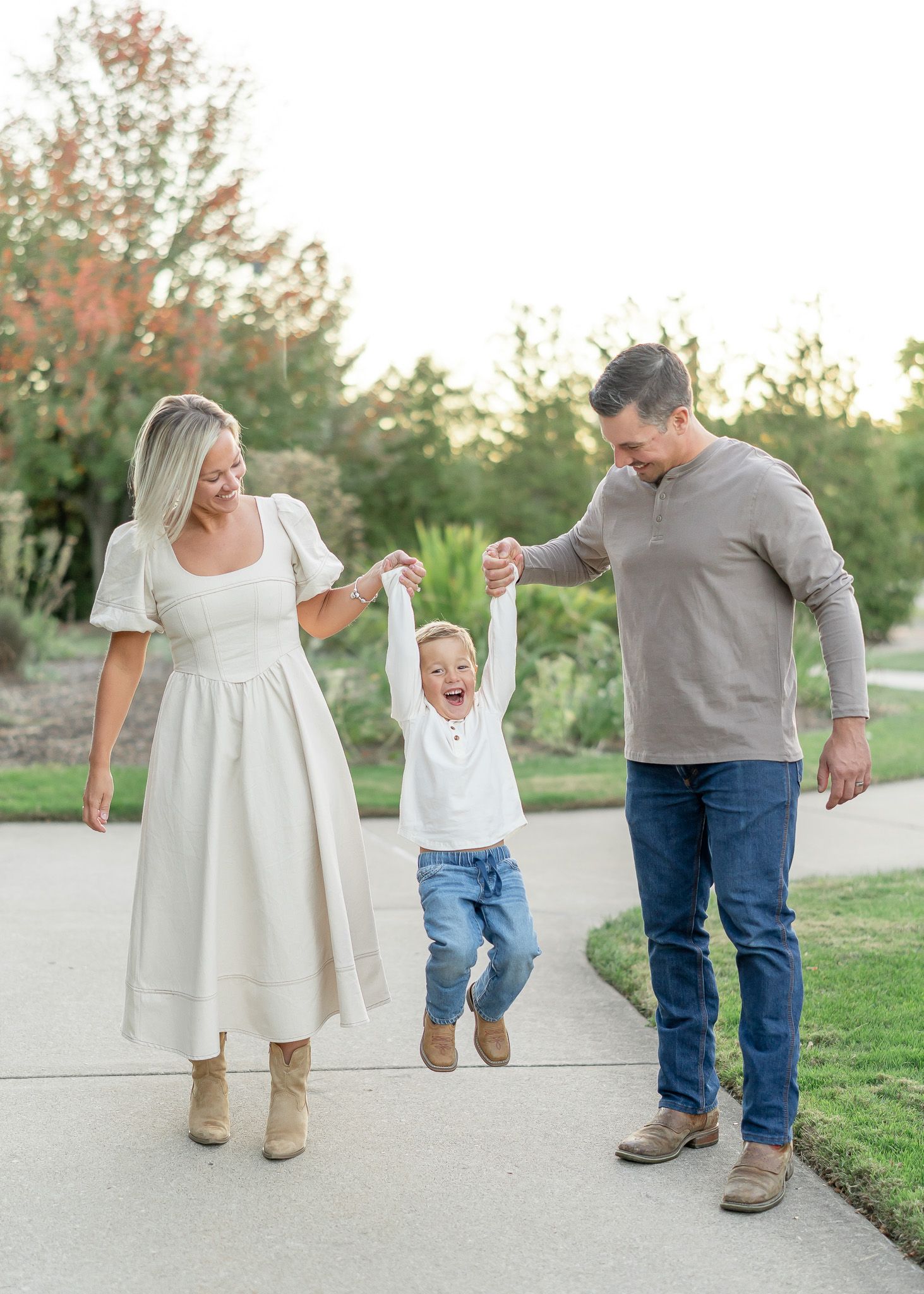 A joyful moment captured outdoors as a small child jumps while holding hands with two adults on a paved walkway.