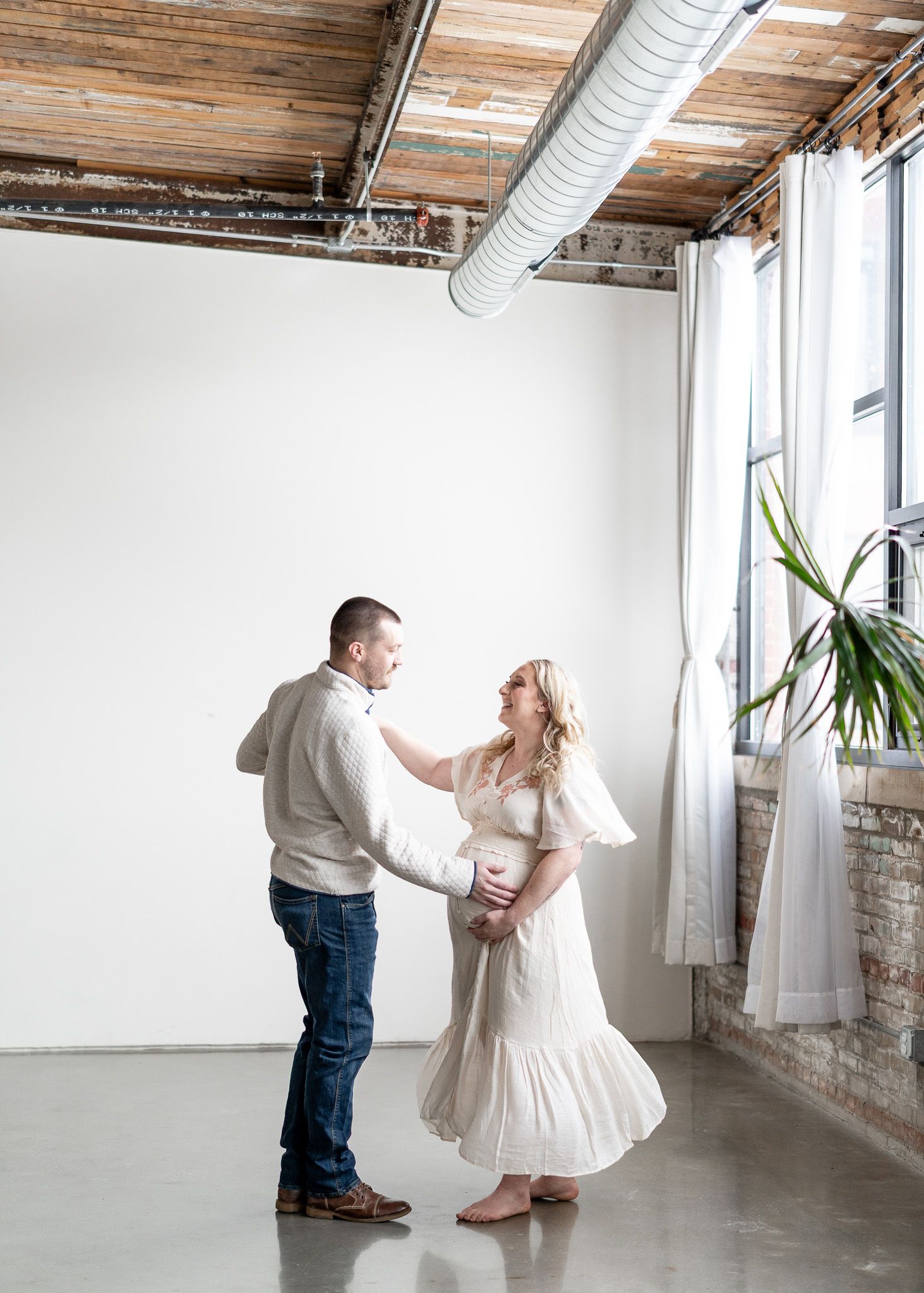 A couple in a rustic loft space dance together, with exposed brick walls and industrial elements visible in the background.