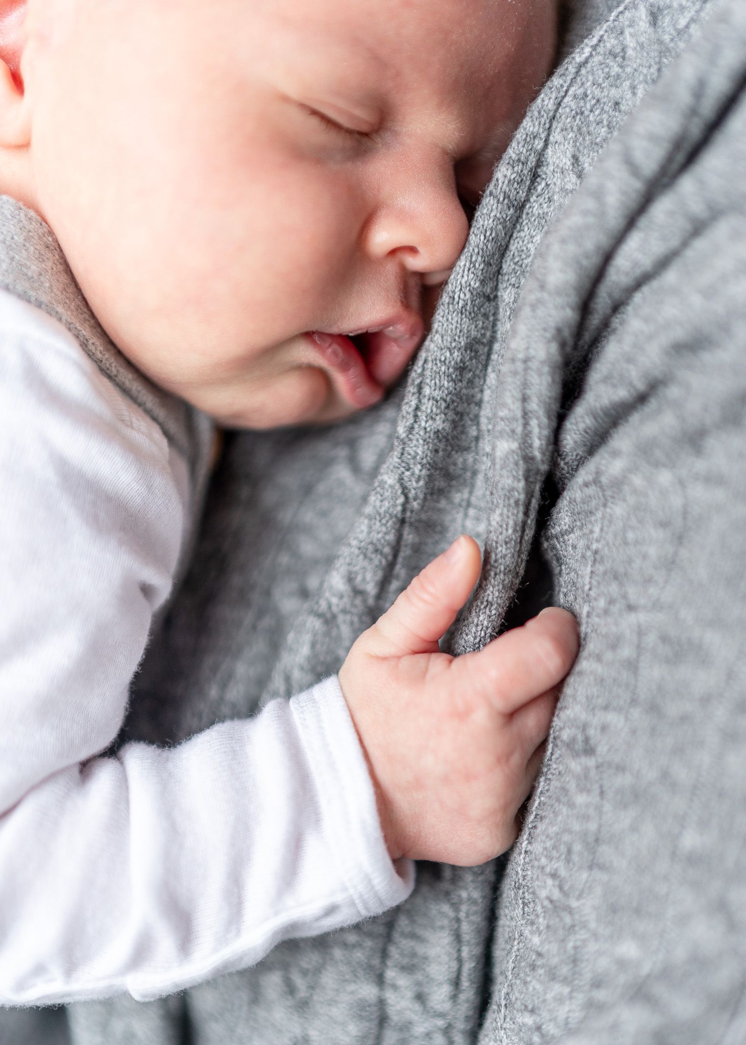 A sleeping baby in white clothing gently rests against a soft gray blanket.