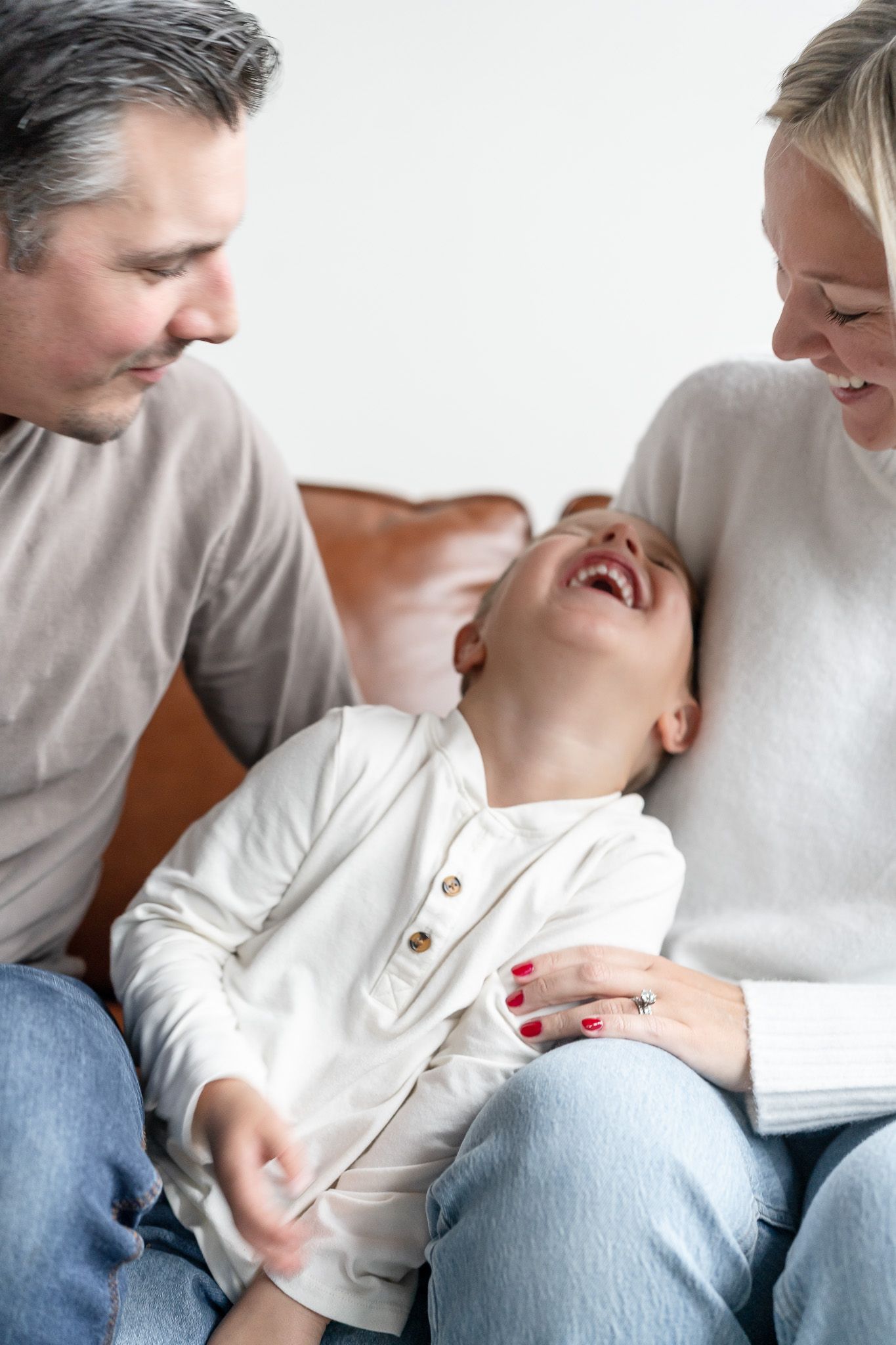 A tender moment between parent and baby as they sit together in casual clothing against a white background.