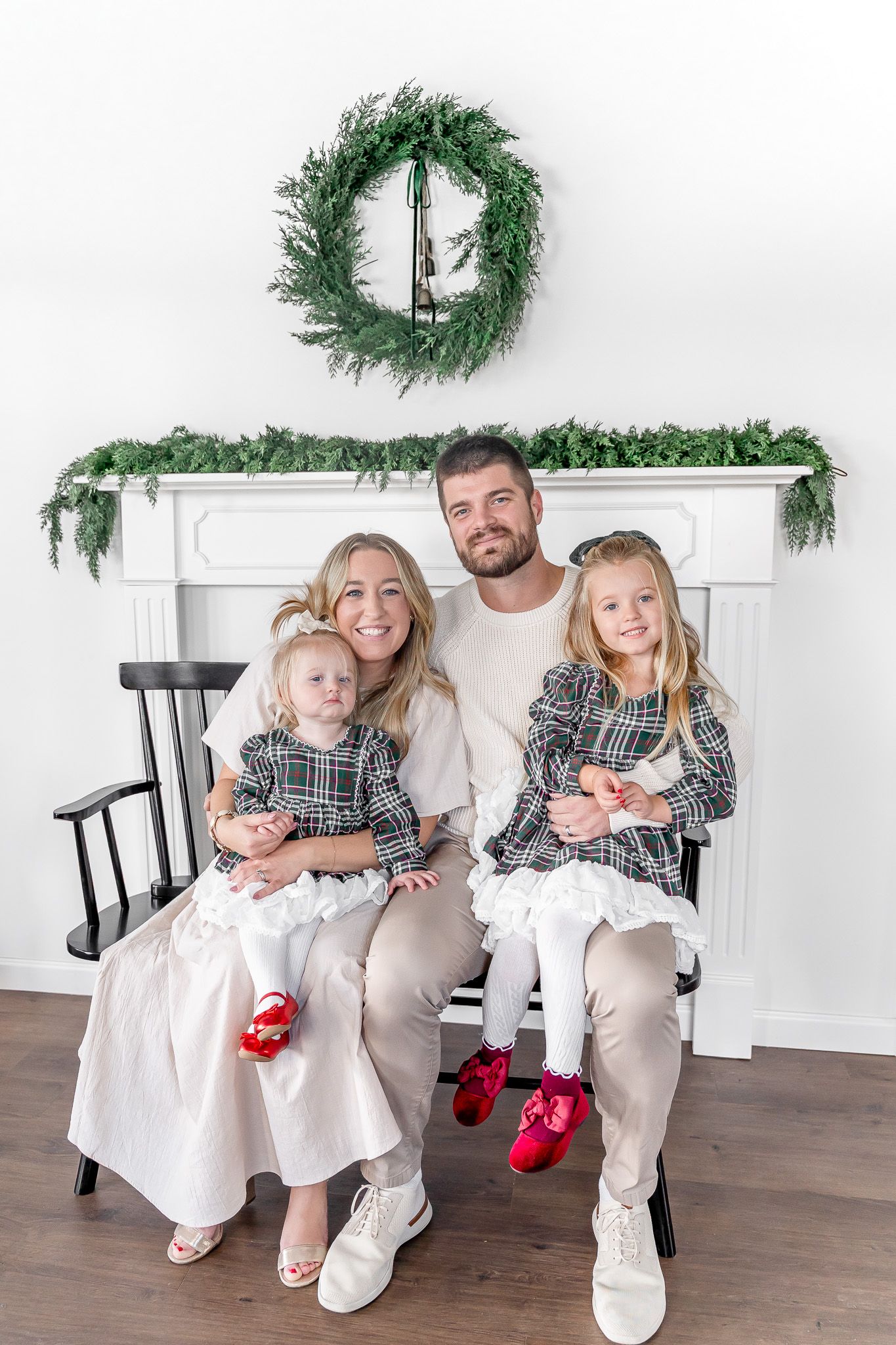 Candid family portraits on black bench with Christmas wreaths and garland in background.