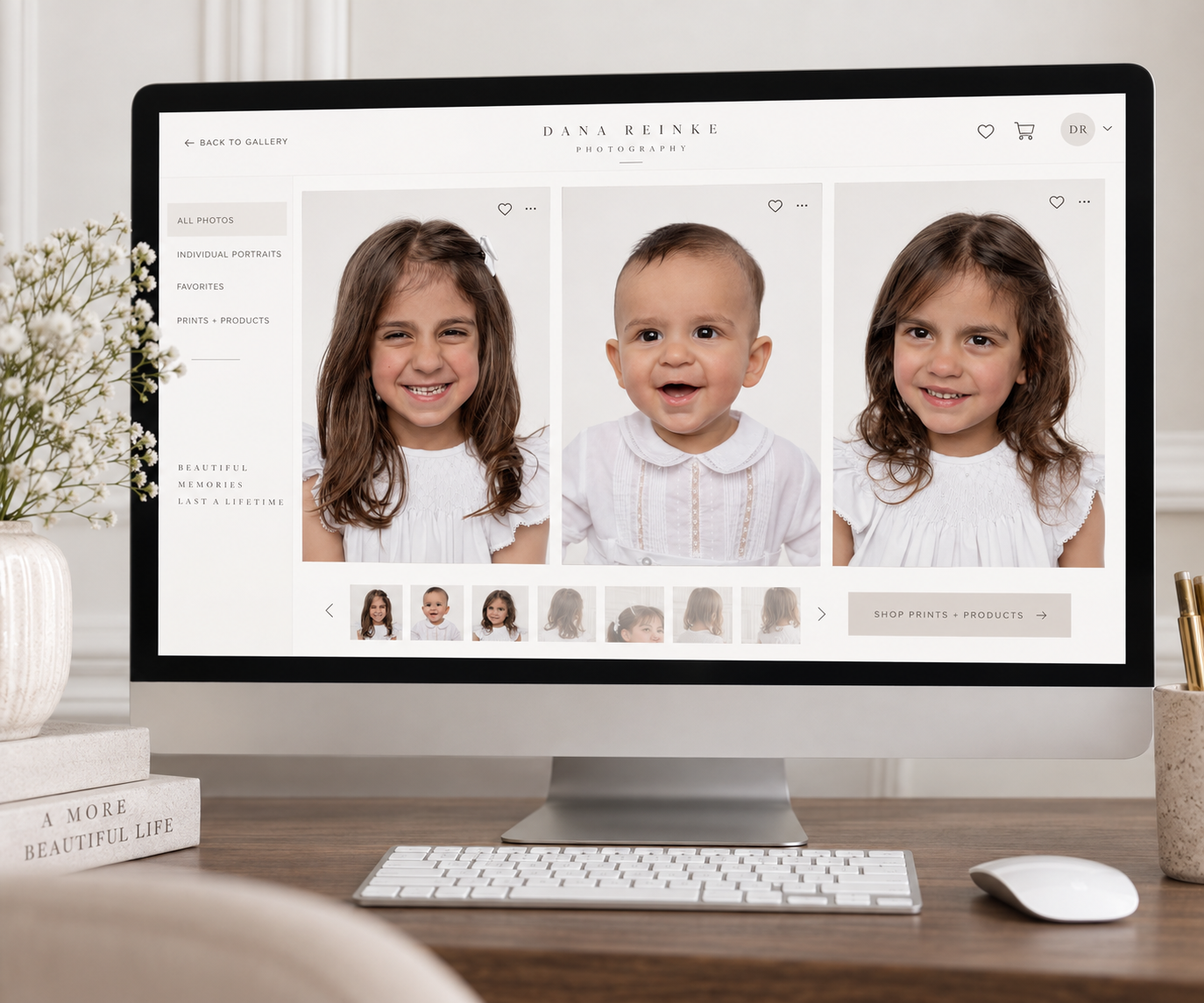 A desktop computer displaying a children's portrait photography website with three smiling kids in white outfits on screen.