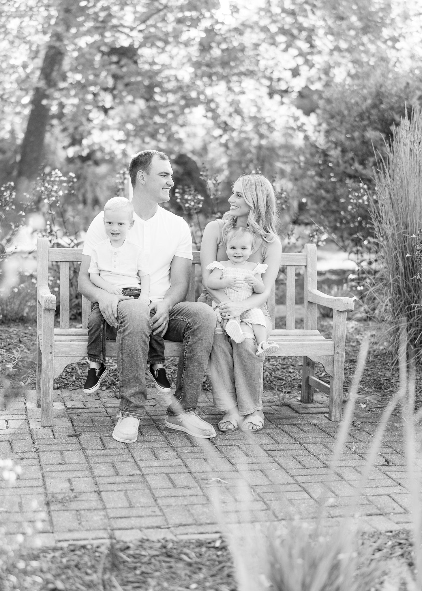 Black and white family portrait series showing candid moments of parents and toddler sitting on outdoor patio chairs.